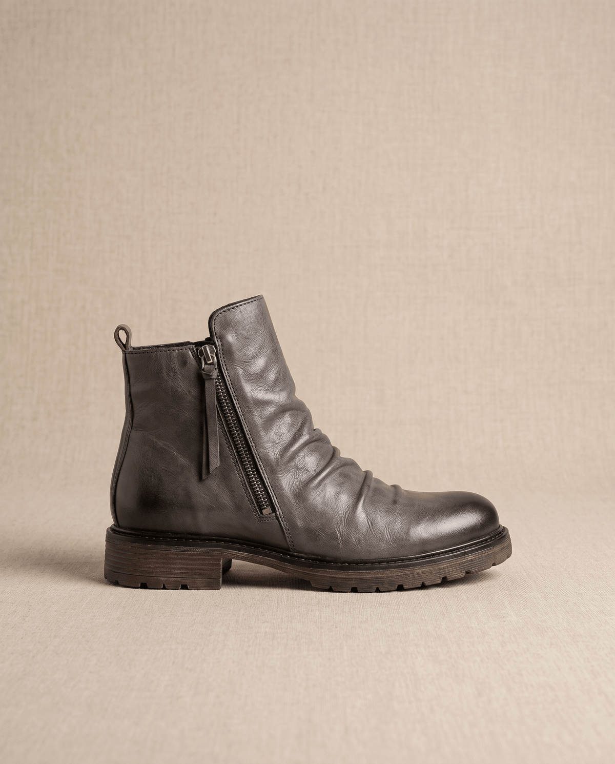 Dark gray waxed leather ankle boots with a ruched shaft, side zip closure, and a rugged, slip-resistant rubber outsole.