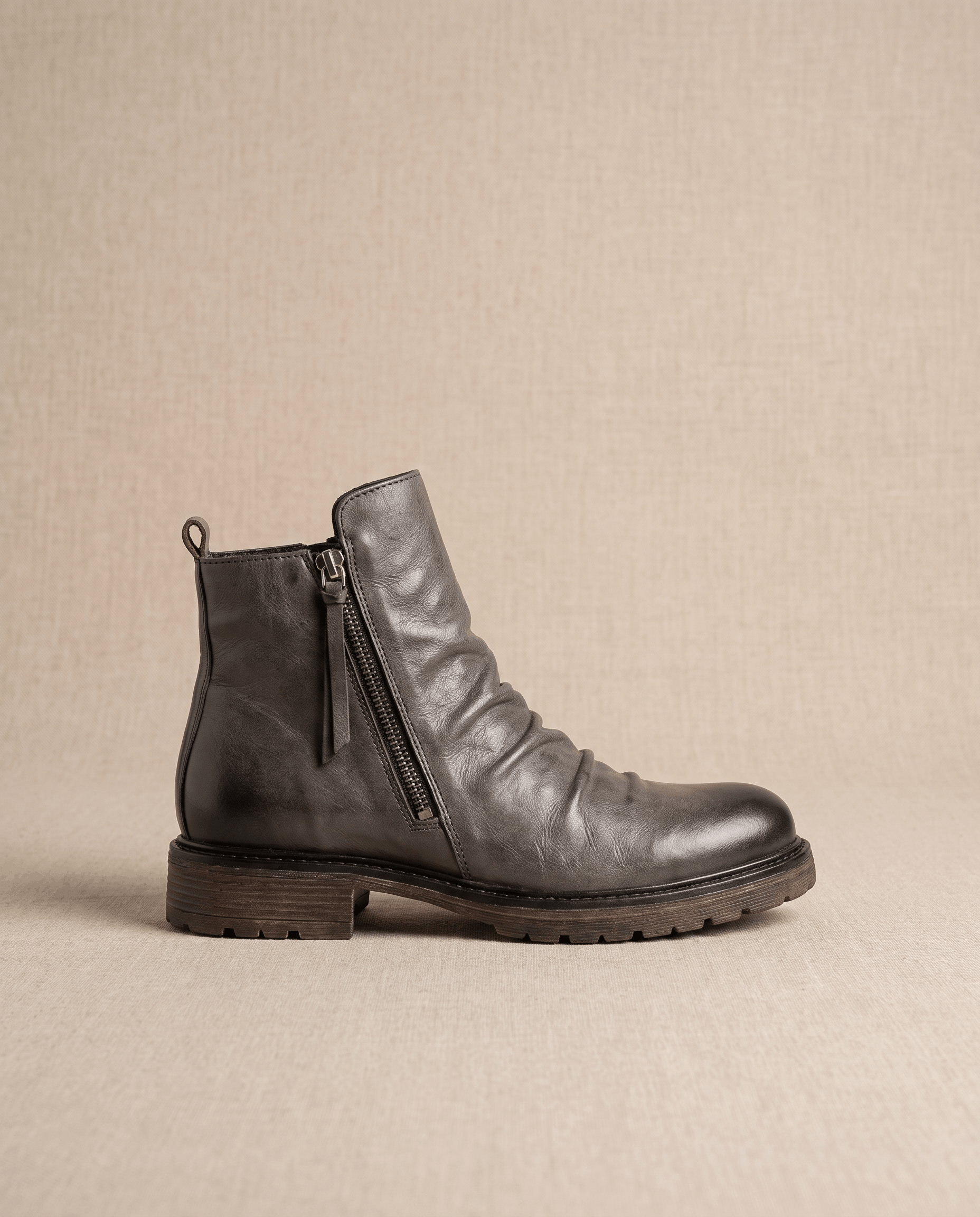 Dark gray waxed leather ankle boots with a ruched shaft, side zip closure, and a rugged, slip-resistant rubber outsole.