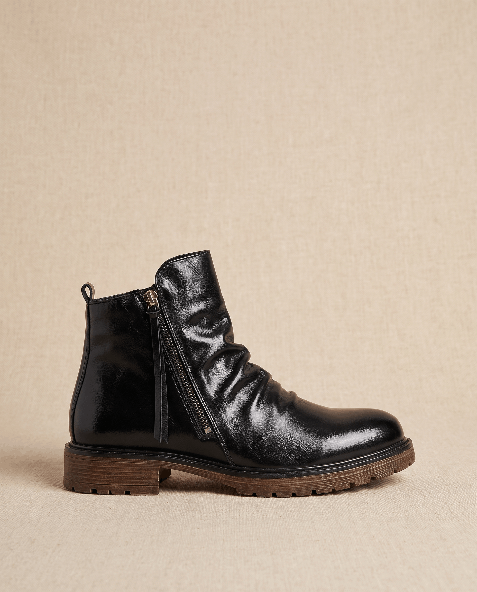 Black waxed leather ankle boot with a ruched shaft, side zip closure, and a rugged, slip-resistant lugged outsole.