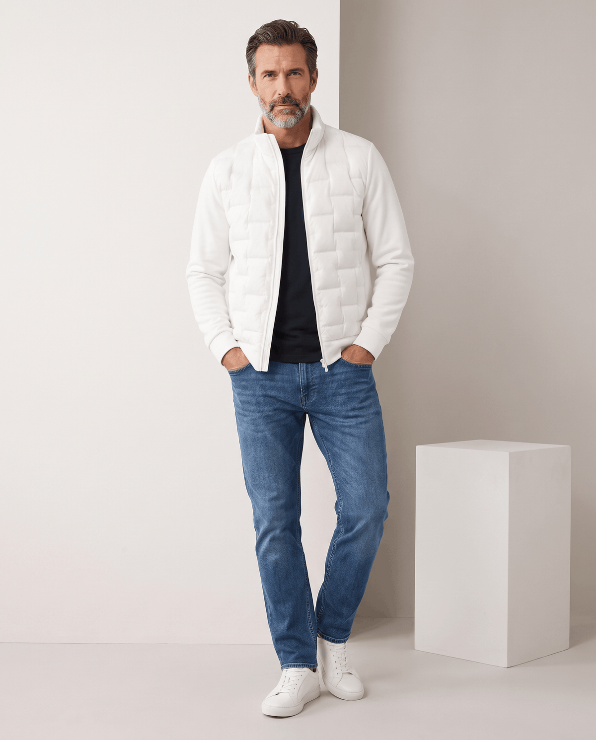 Man standing in a white hybrid puffer jacket with blue jeans, full-length view