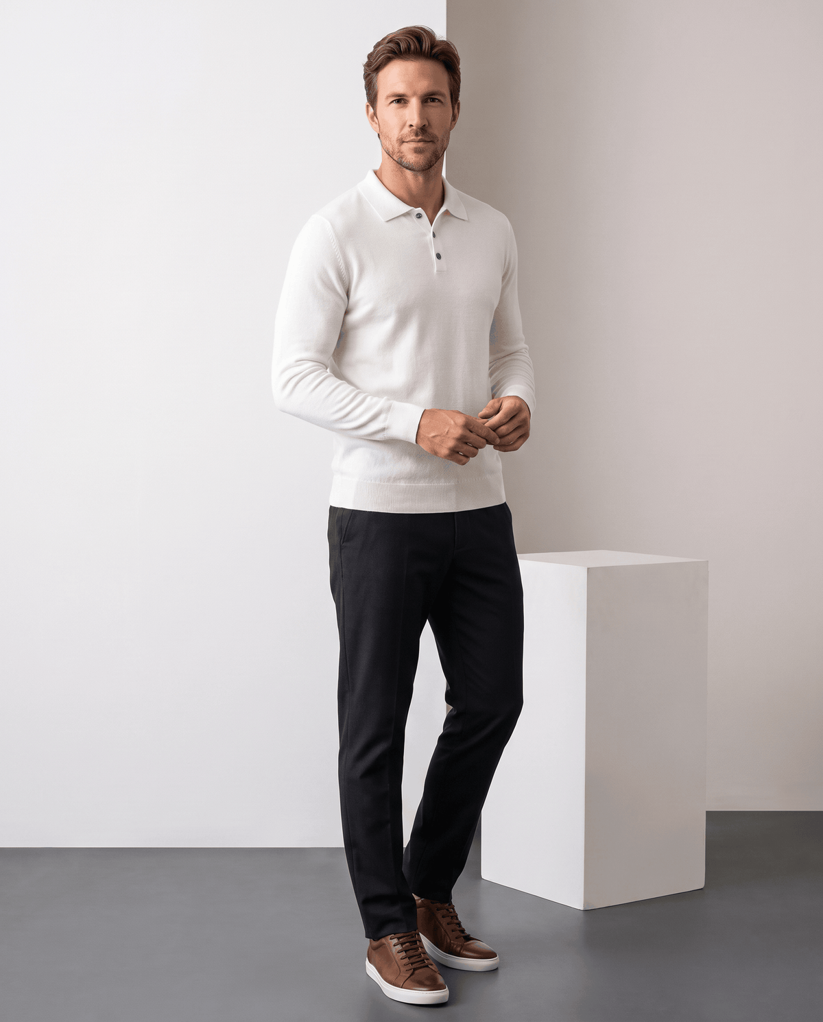 Full-length view of a man wearing the Elias white polo sweater with black trousers