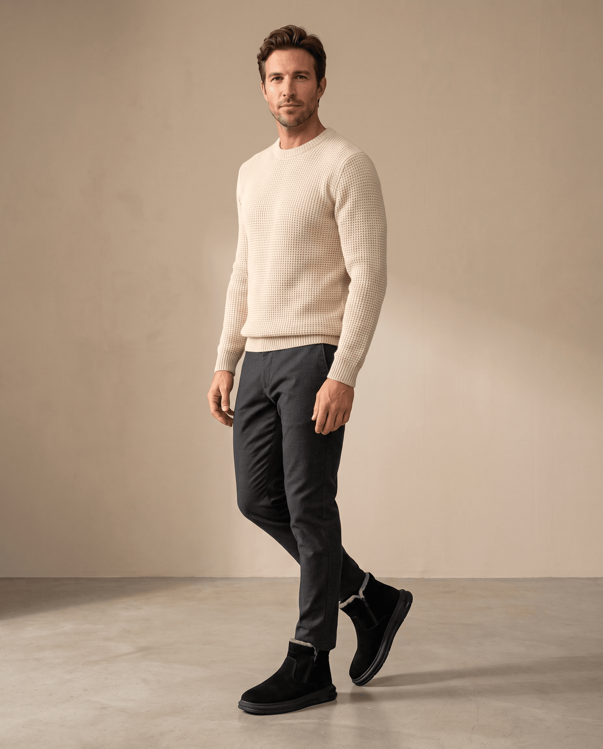 Man wearing black wide toe box winter boots with a beige sweater and dark pants.