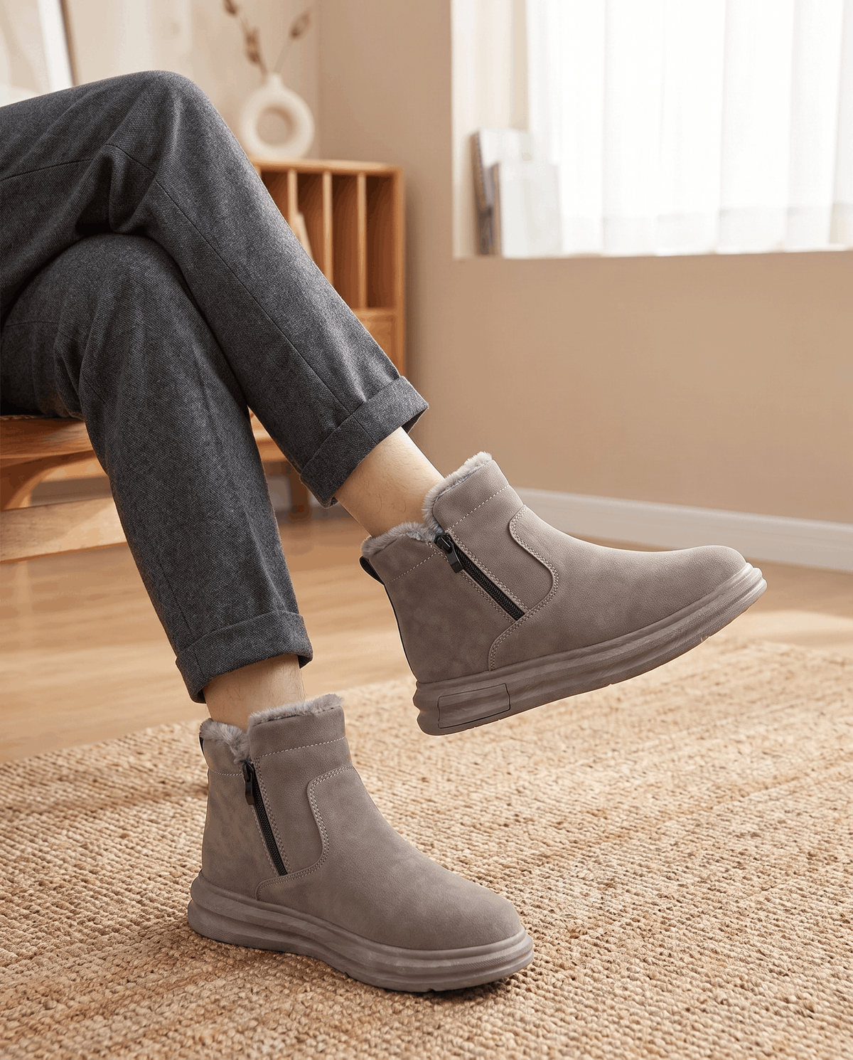 Person wearing taupe fleece-lined winter boots with a wide toe box and dark pants indoors.