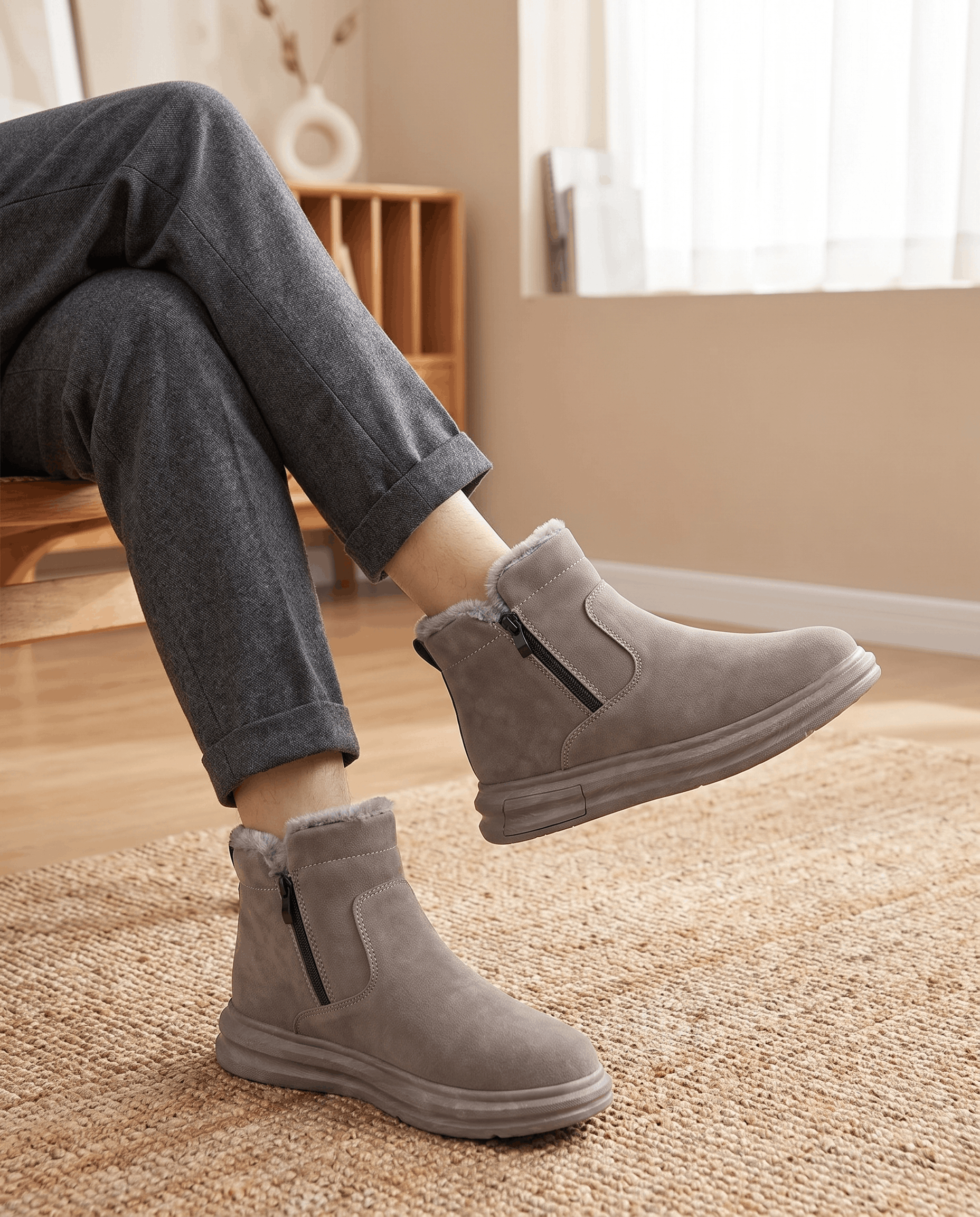 Person wearing taupe fleece-lined winter boots with a wide toe box and dark pants indoors.