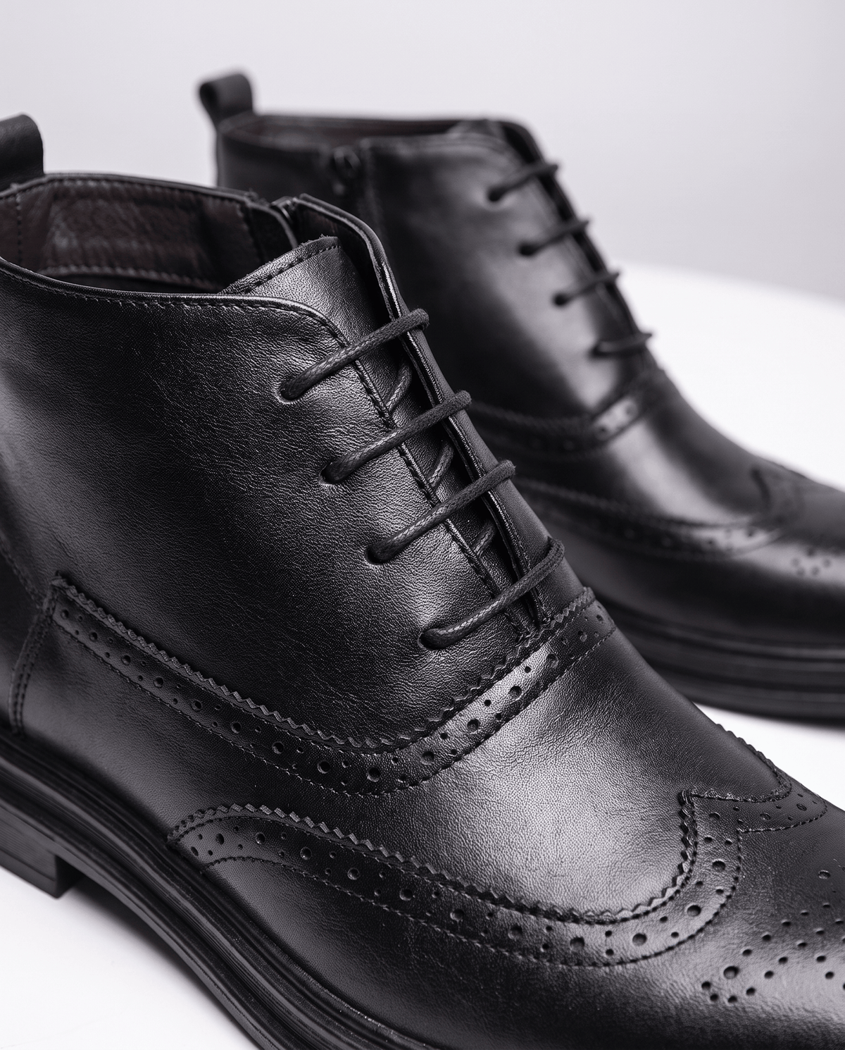Close-up of black brogue perforations and laces on a leather ankle boot