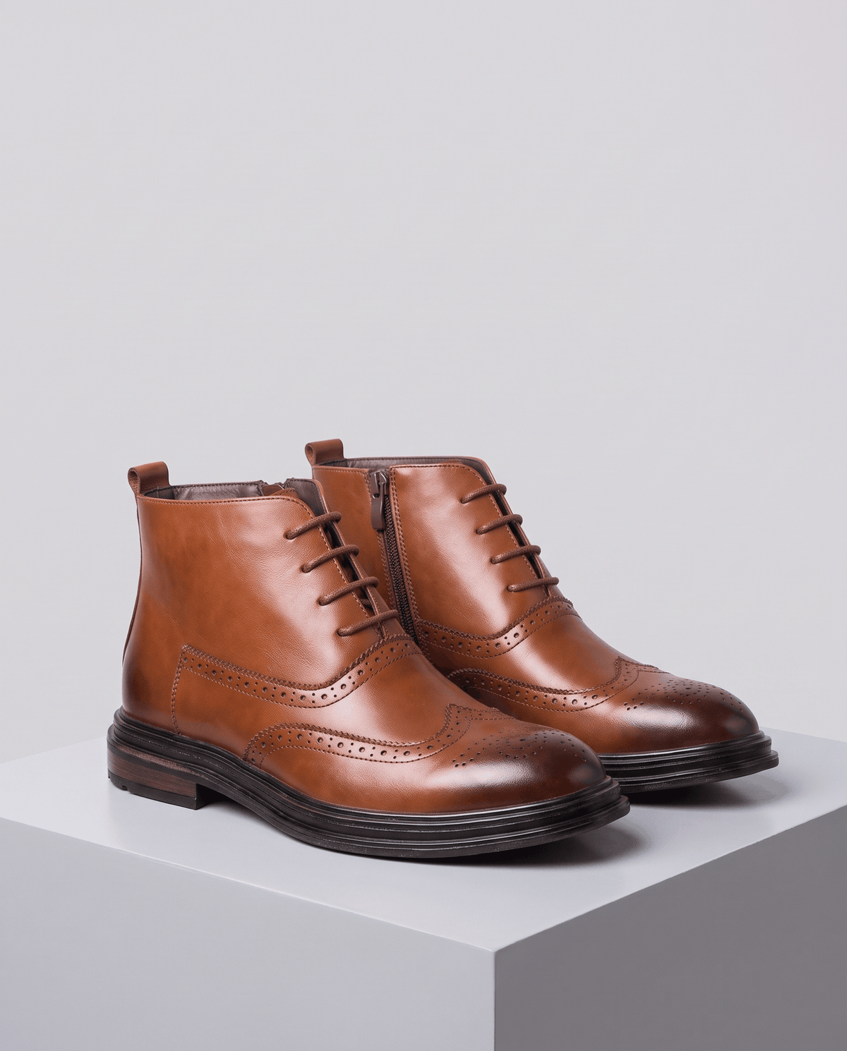 Pair of brown lace-up brogue ankle boots on a gray block