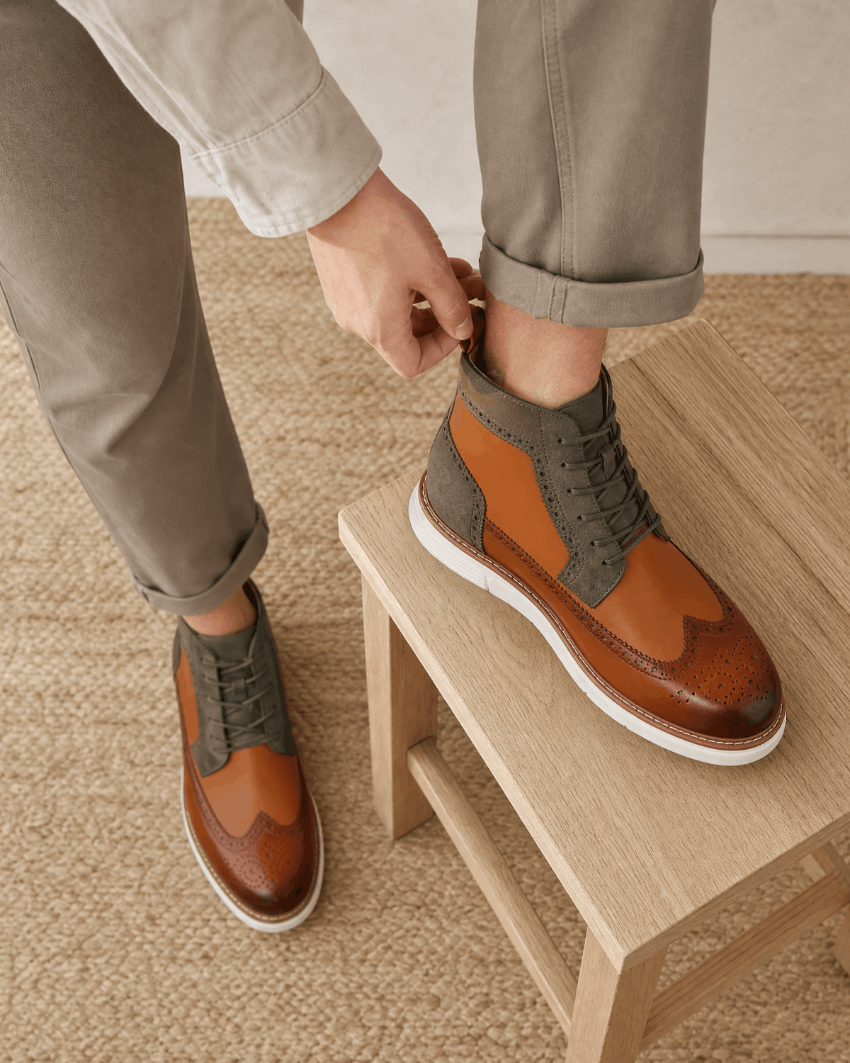 Smooth grain brown leather wingtip boots with matte panels, brogue perforations, and a chunky white cupsole on a stool.