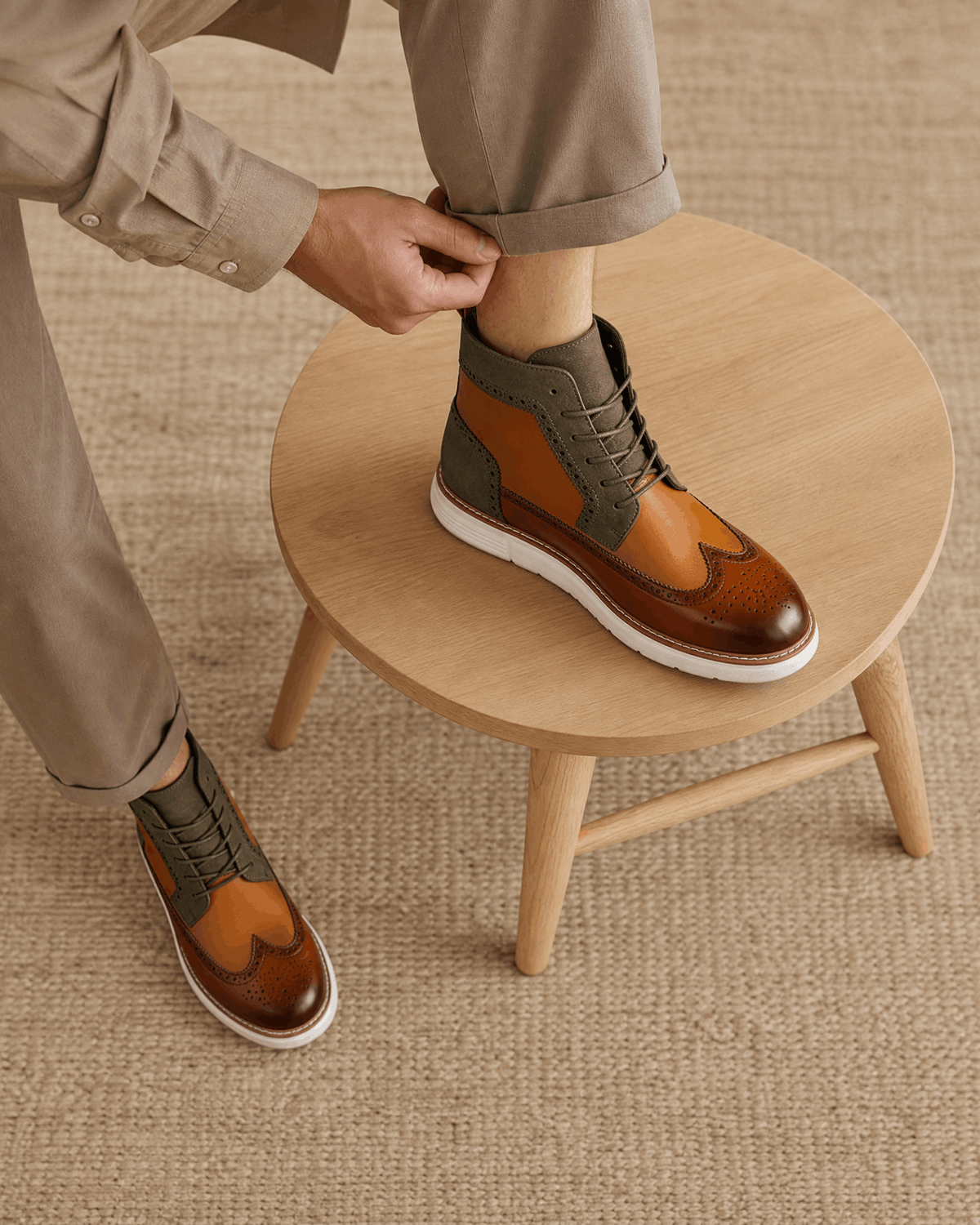 Smooth grain brown wingtip boots featuring brogue perforations, matte panels, and a chunky white cupsole on a wooden stool.