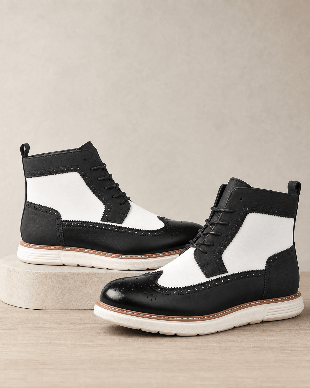 Black and white wingtip boots featuring brogue perforations, matte panels, and a chunky white cupsole with a stitched welt.