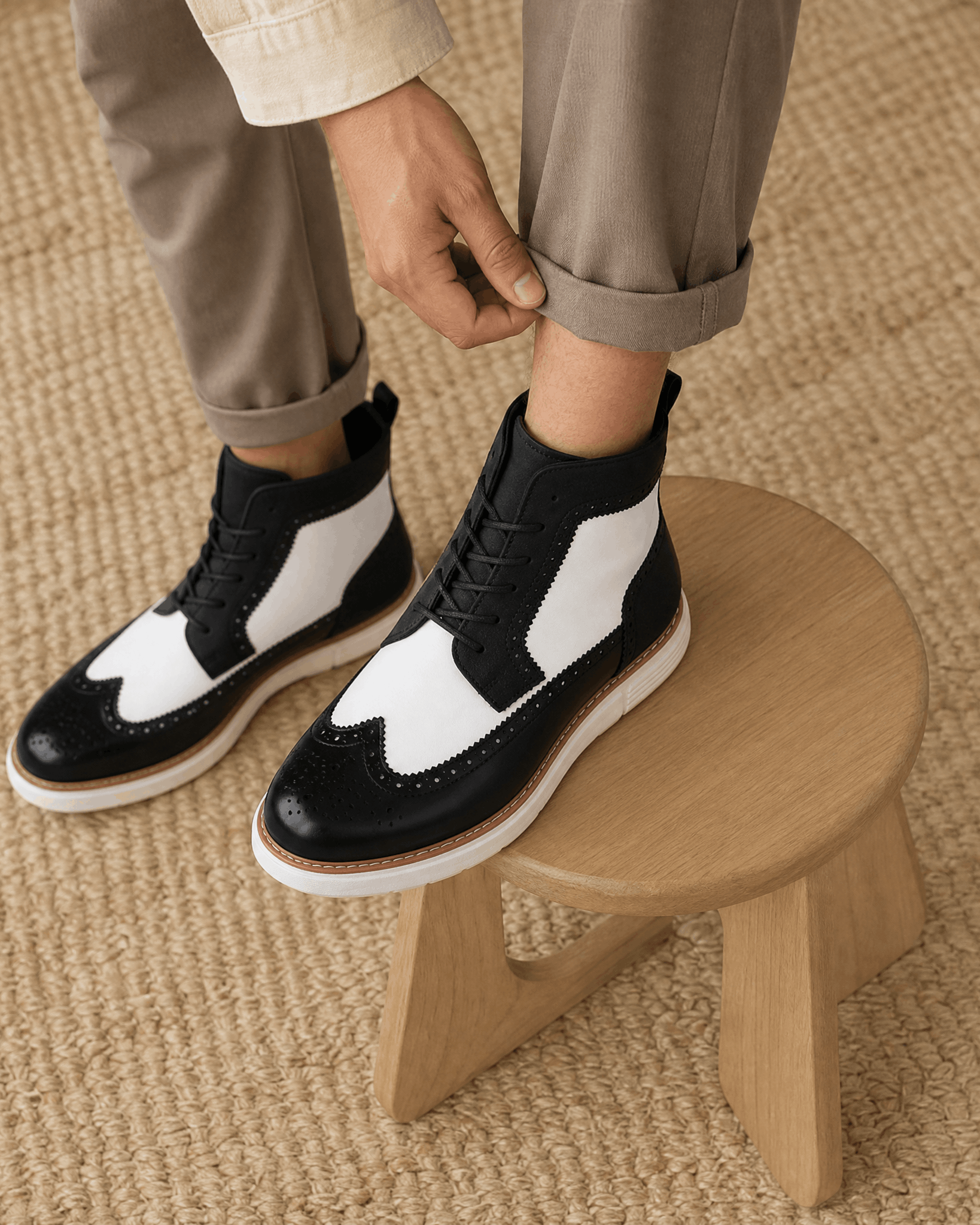 Black and white wingtip brogue boots with matte panels, lace-up front, and a chunky white cupsole on a wooden stool.