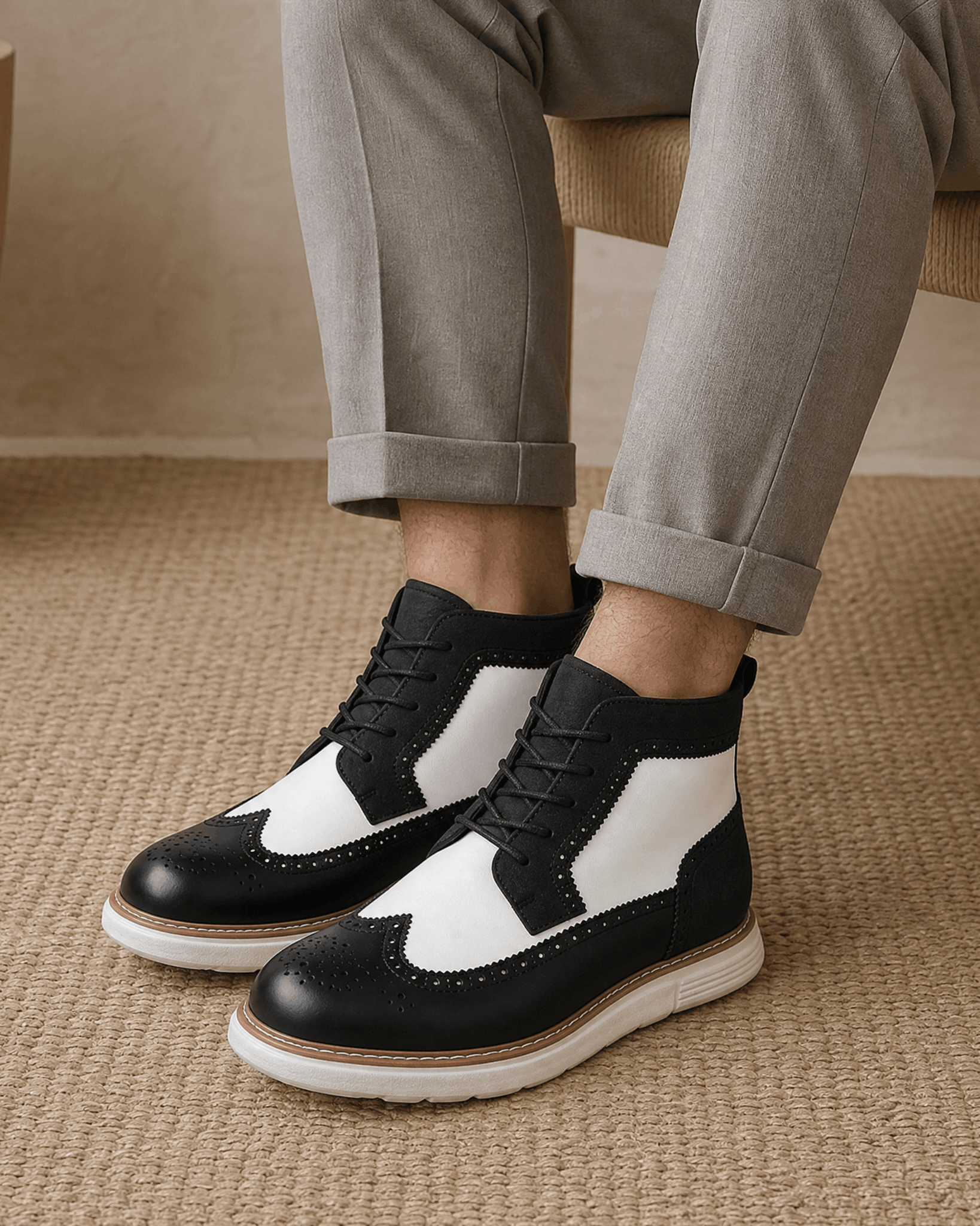 Black and white wingtip brogue boots with matte panels, lace-up front, and a chunky white cupsole worn with grey trousers.