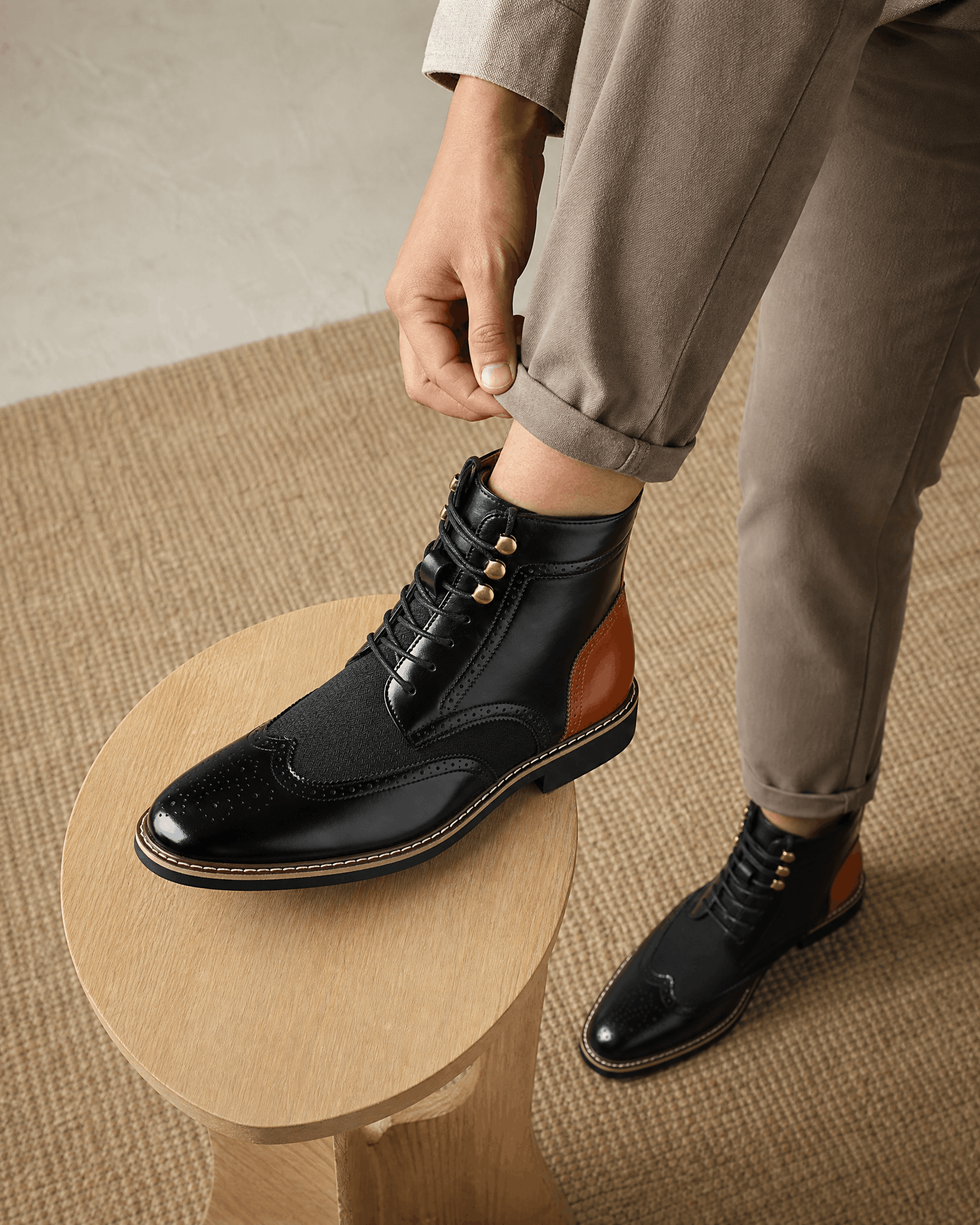 Black smooth grain leather ankle boots with wingtip brogue details, woven panels, metal eyelets, and a stacked block heel.