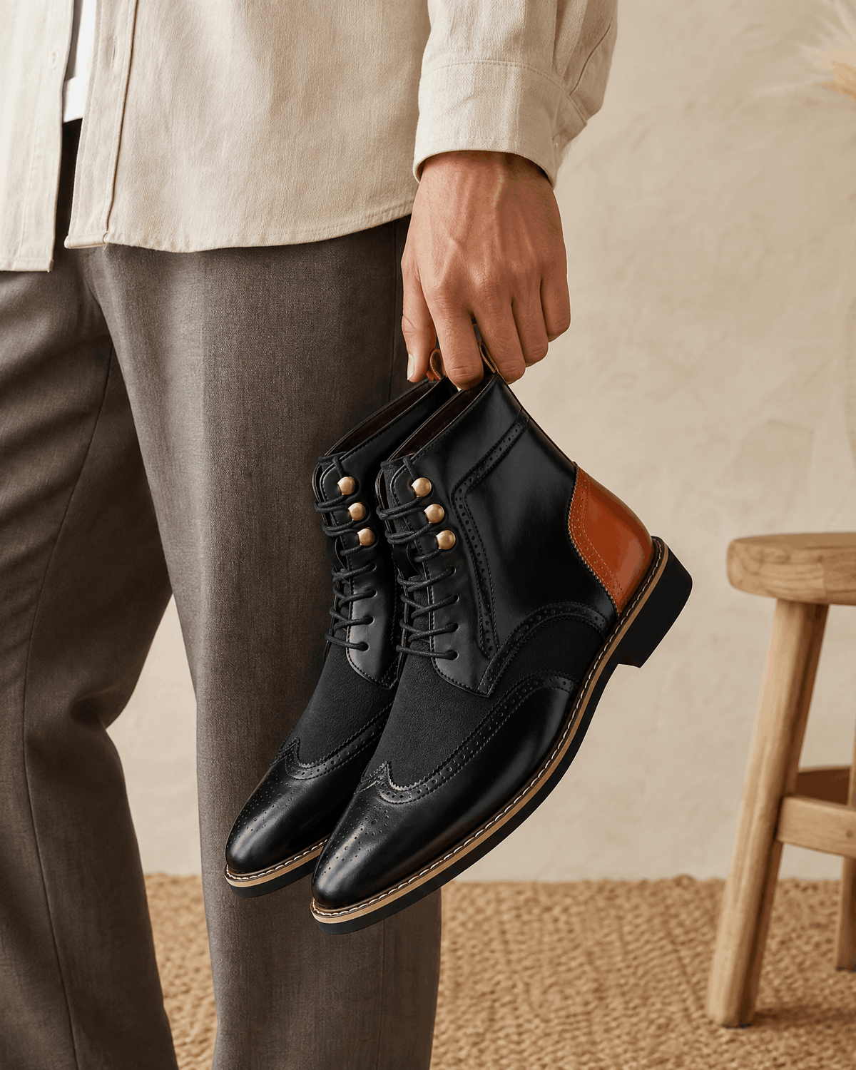 Black smooth grain leather ankle boots with wingtip brogue detailing, metal eyelets, and a contrast tan heel panel.