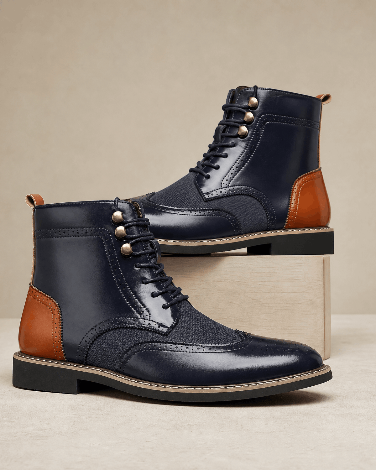 Navy blue and tan leather wingtip brogue ankle boots with woven-texture panels, metal eyelets, and a stacked block heel.
