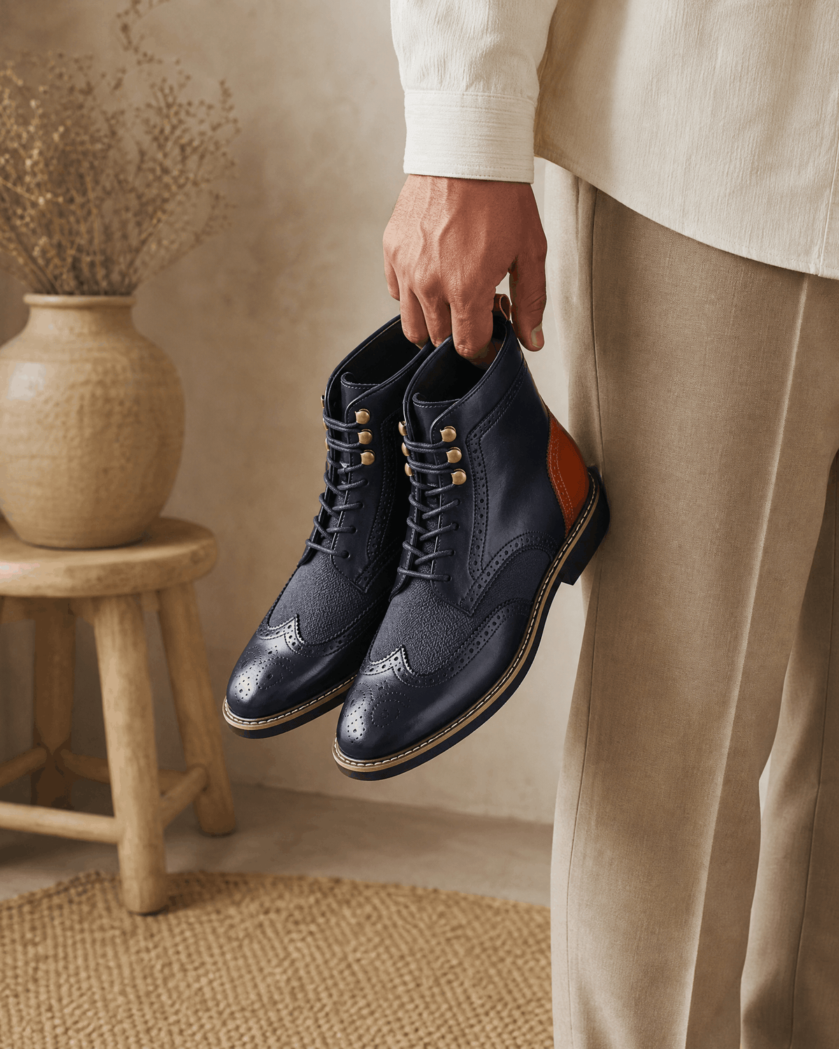 Navy smooth grain leather ankle boots with wingtip brogue detailing, woven-texture panels, and gold metal eyelets.
