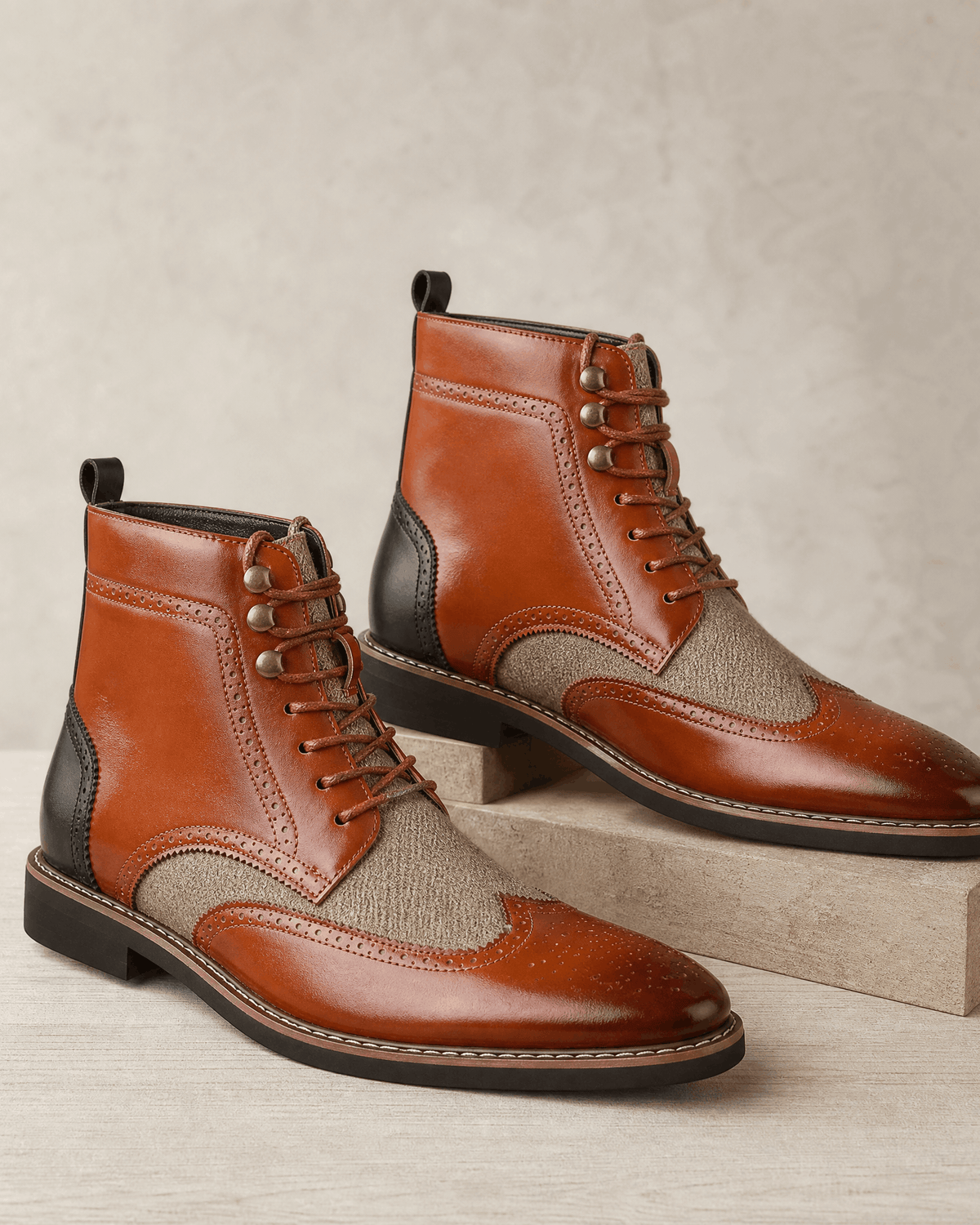 Tan smooth grain leather ankle boots with wingtip brogue perforations, woven-texture panels, and metal eyelet lace-up closures.