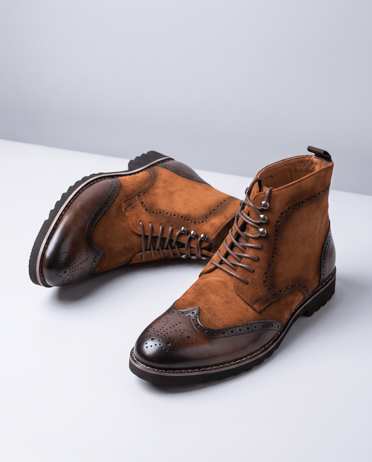 Pair of brown lace-up brogue boots angled on a pale gray surface