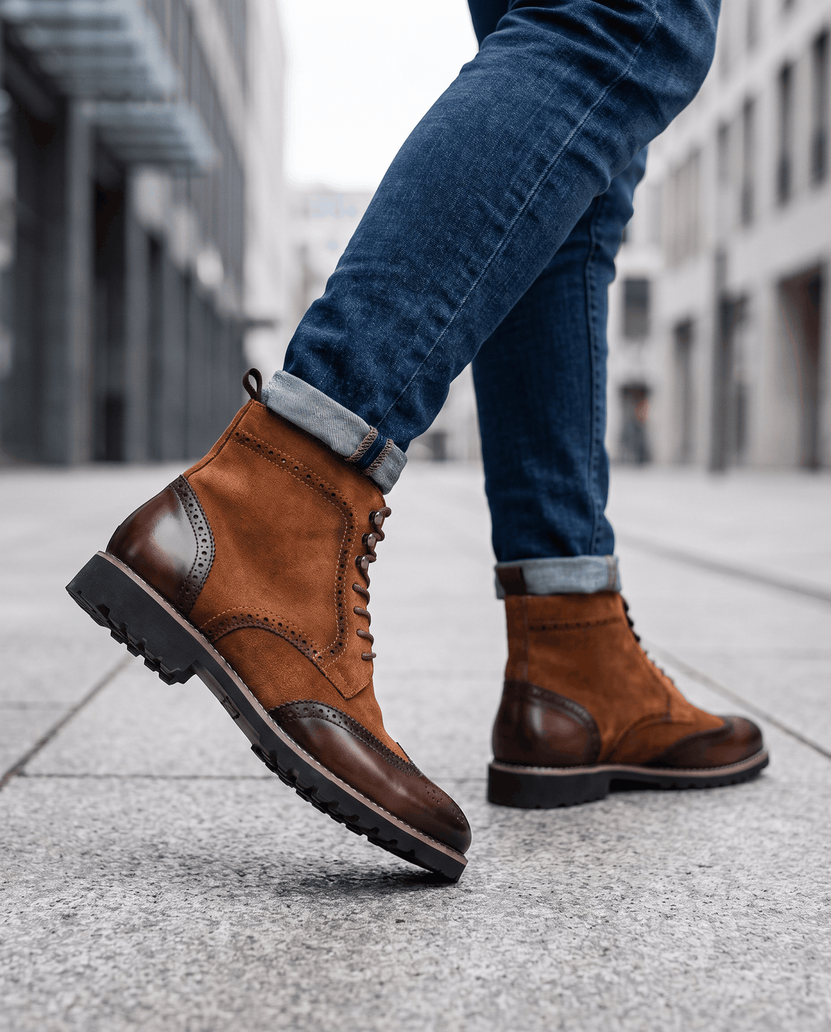 Man in rolled blue jeans and brown wingtip boots walking on a paved street