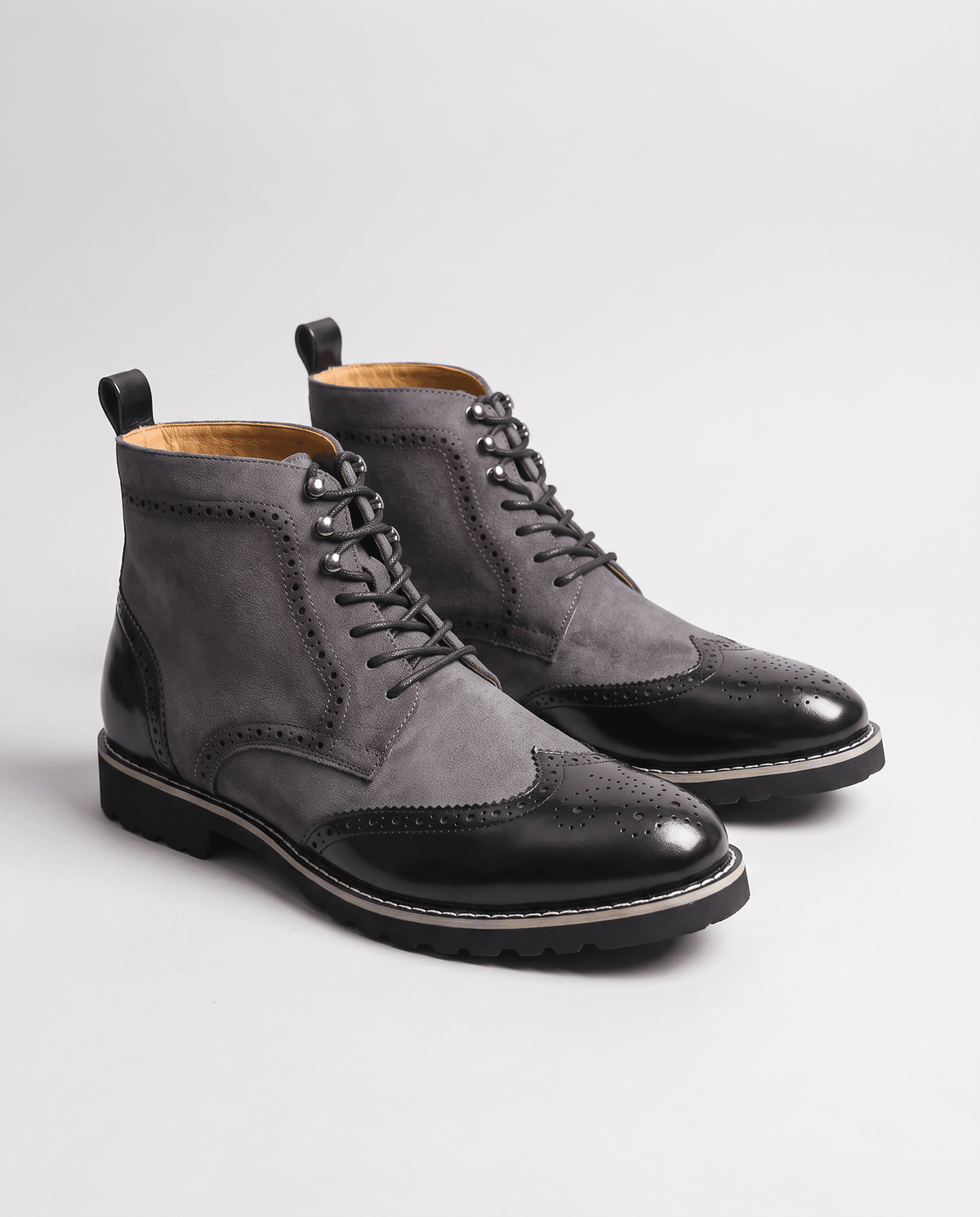 Pair of gray suede brogue boots with black toe caps on a light background