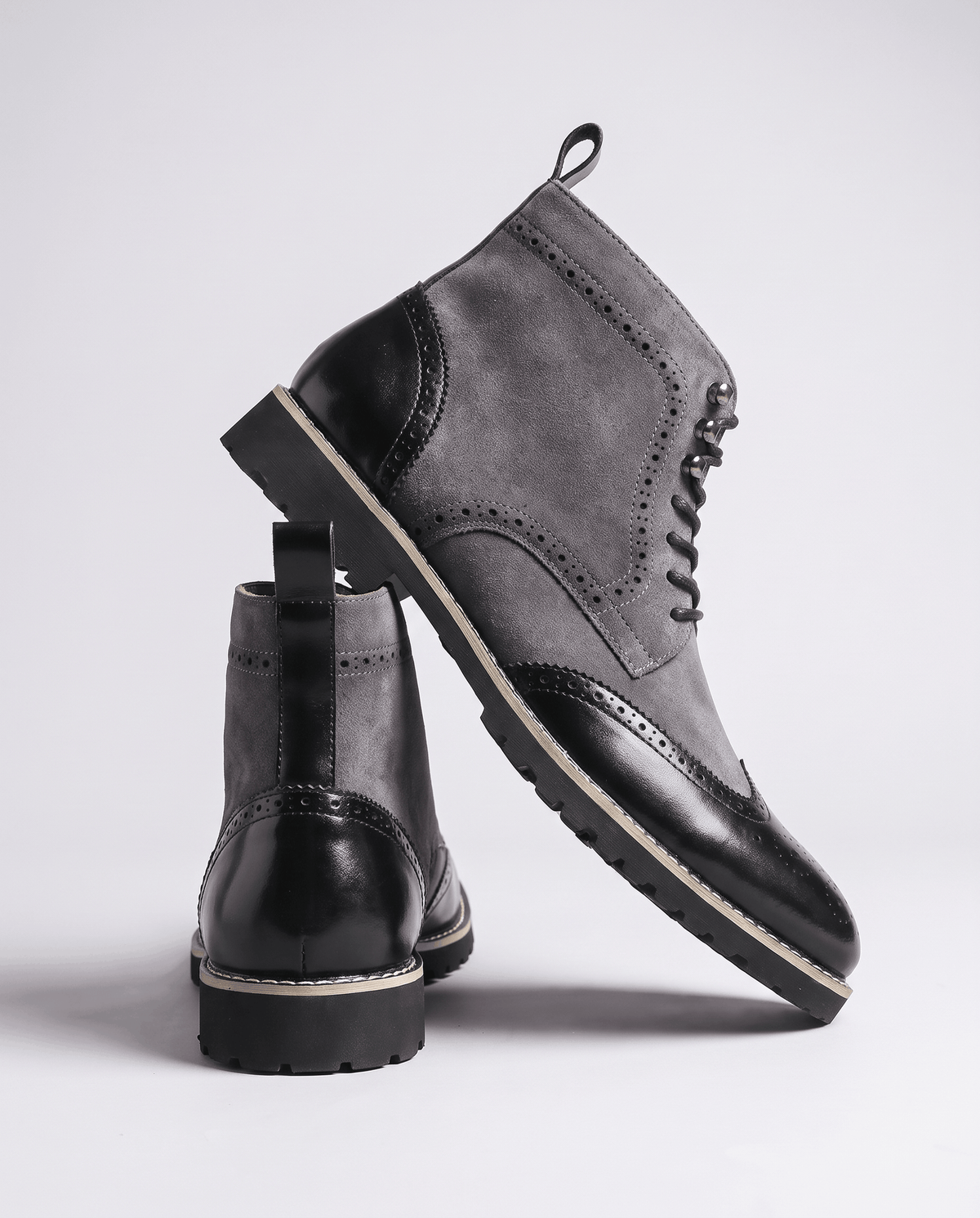 Gray suede boot tilted to show the rubber sole, with a second boot standing behind