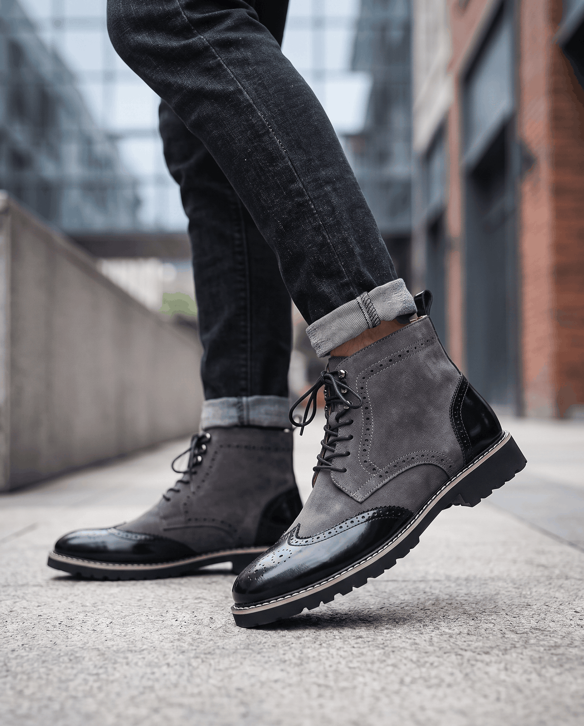 Man in gray suede wingtip boots and dark trousers standing on a city pavement