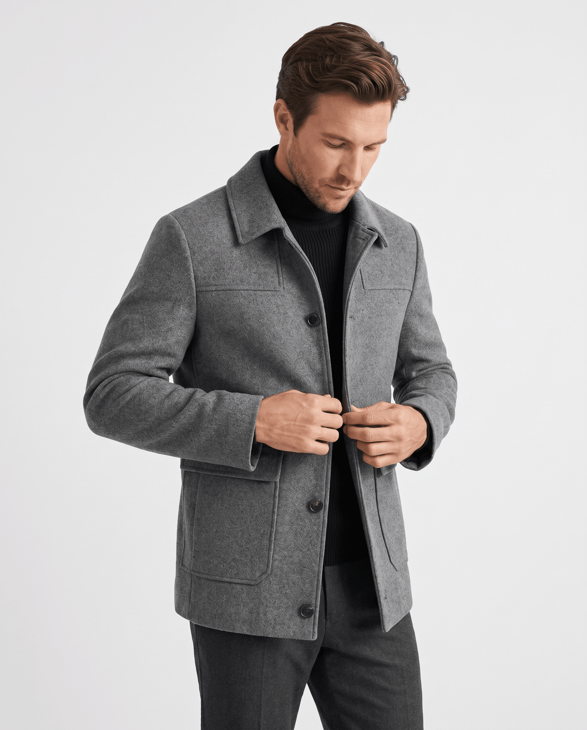 Model fastening a mid-chest button on the gray coat, lapel folded flat