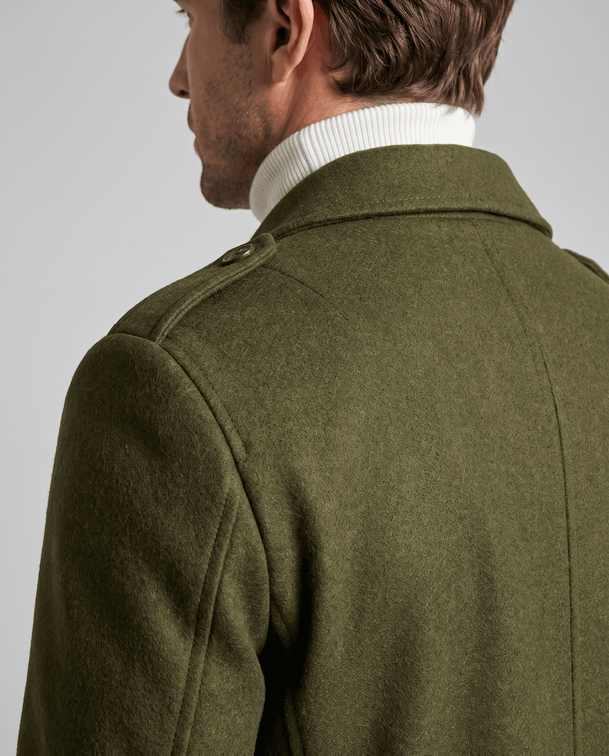 Back view of the army green overcoat's collar and shoulders, worn over a white turtleneck