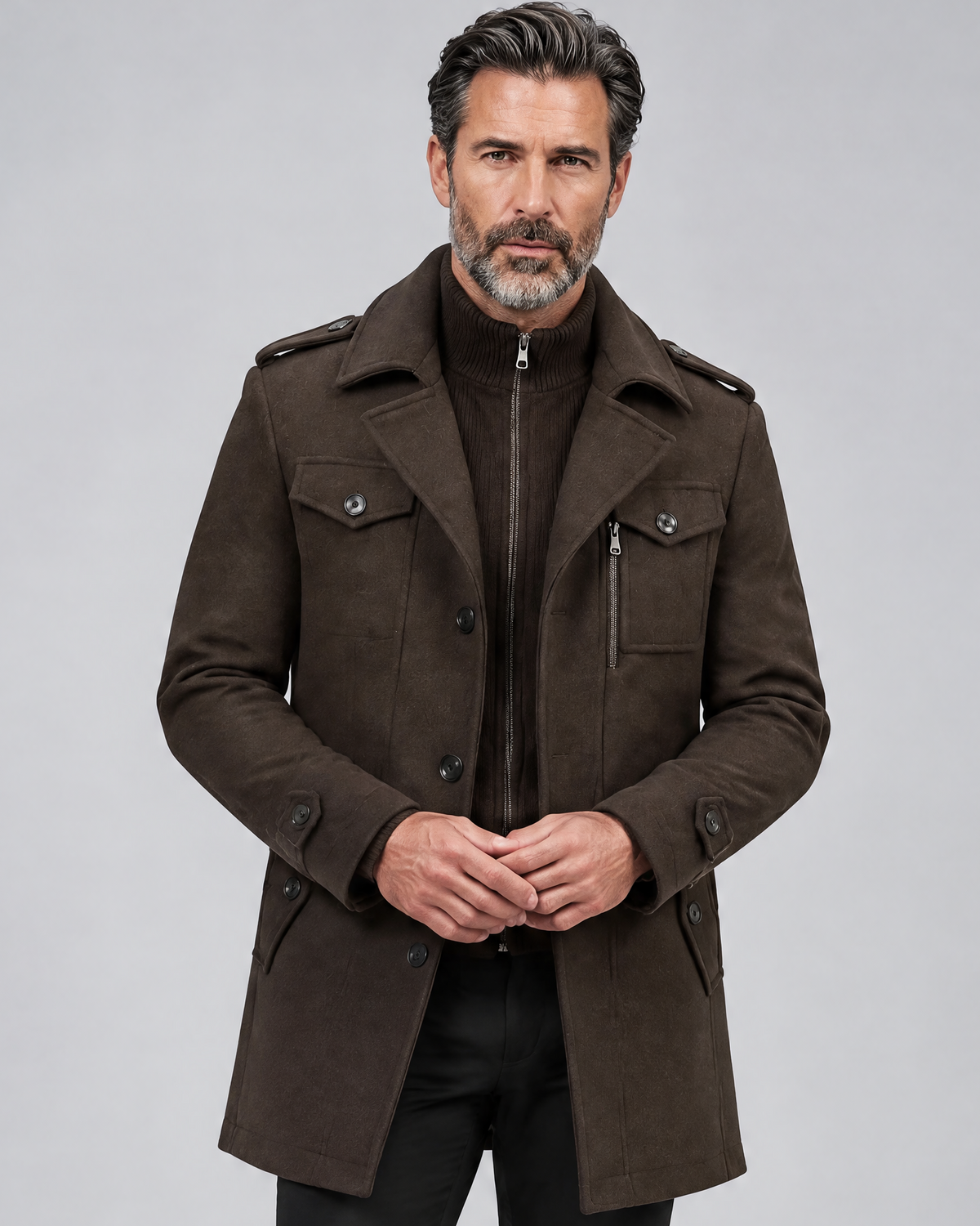 Brown military-style coat worn buttoned with a knit bib, hands clasped at the waist, front view