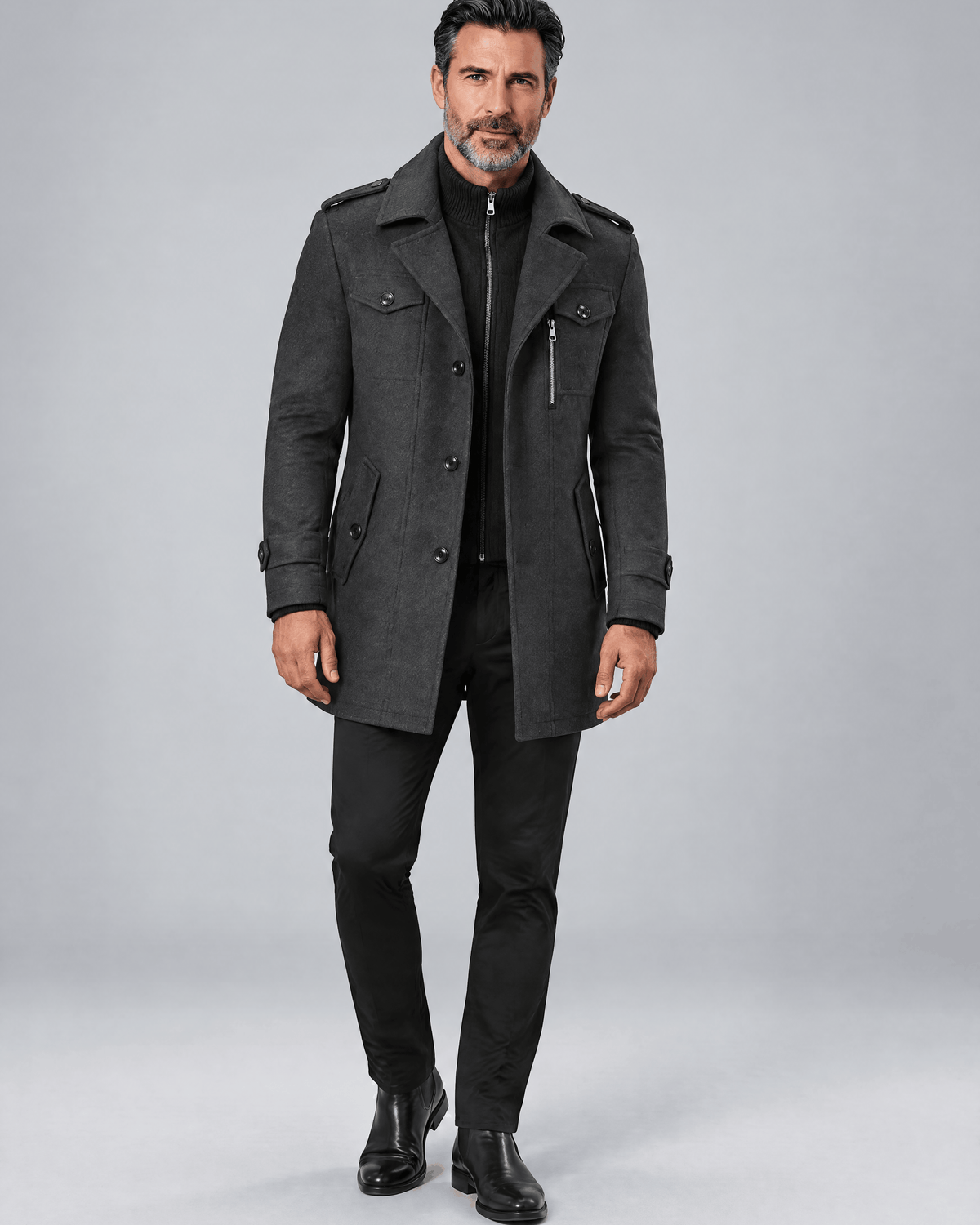 Gray military-style coat worn buttoned over dark trousers and shoes, full-length front view