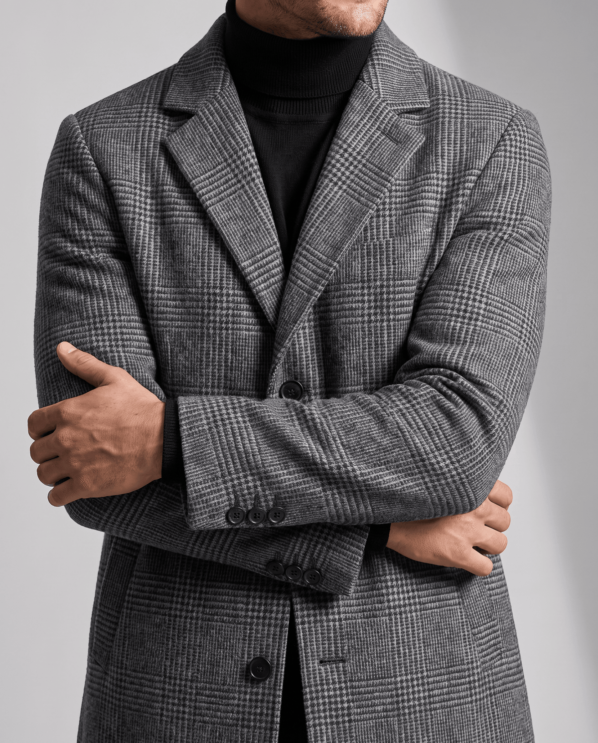 Gray check overcoat front detail with notch lapel and button front, worn over a dark turtleneck