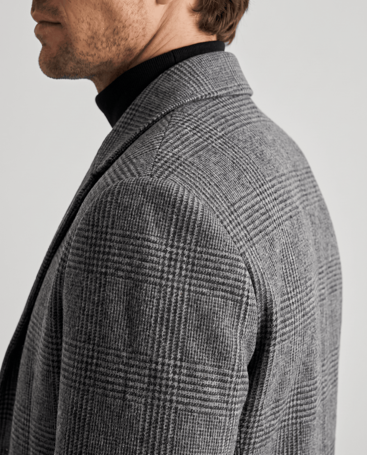 Side close-up of the gray overcoat's check weave and notch lapel over the shoulder
