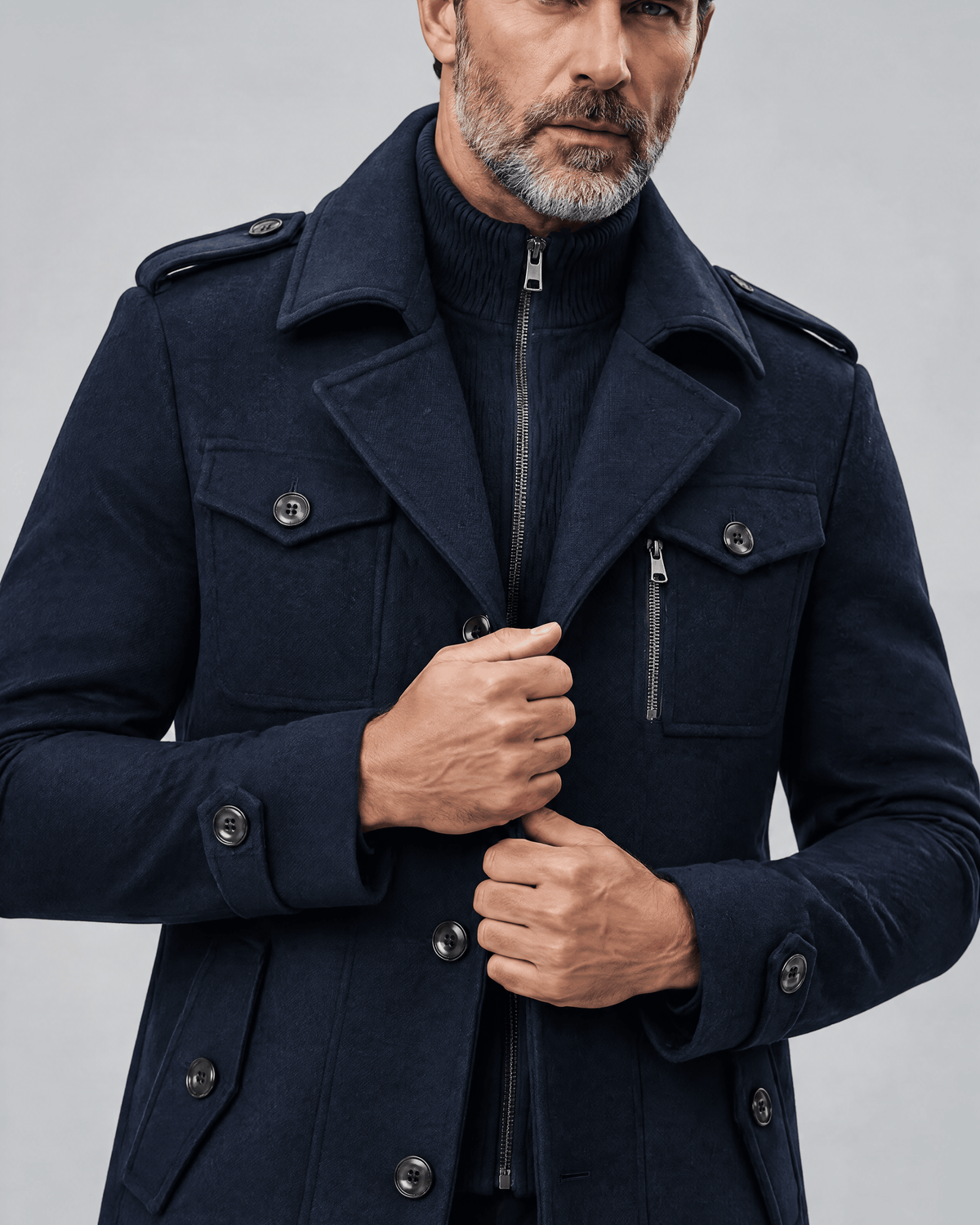 Close-up of the navy coat's zip bib, chest pocket flaps and epaulettes with hands at the front