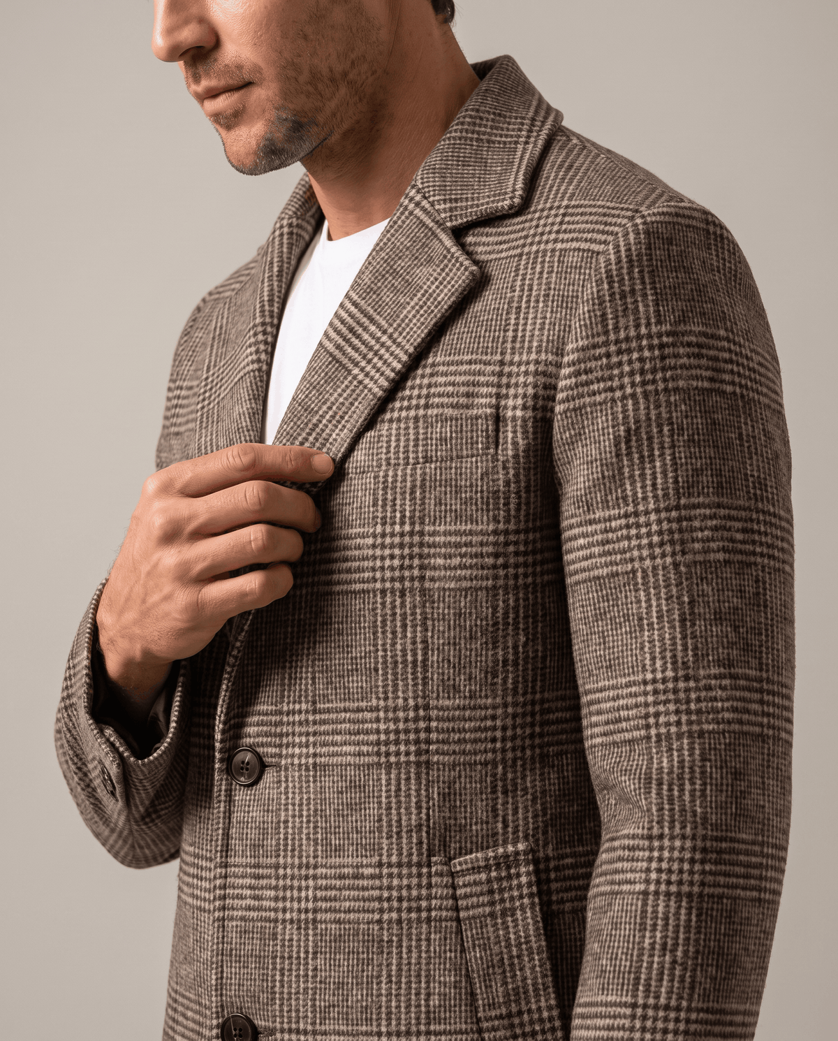 Taupe overcoat notch lapel and button front, with one hand adjusting the collar