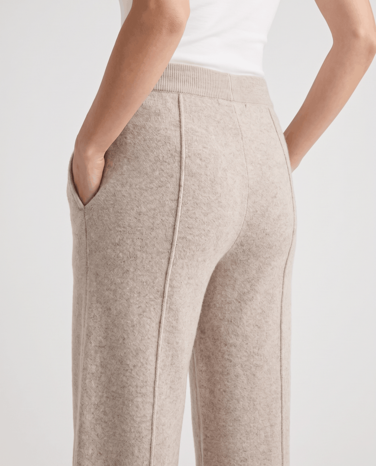 Back detail of beige knit pants with seam and hands in pockets