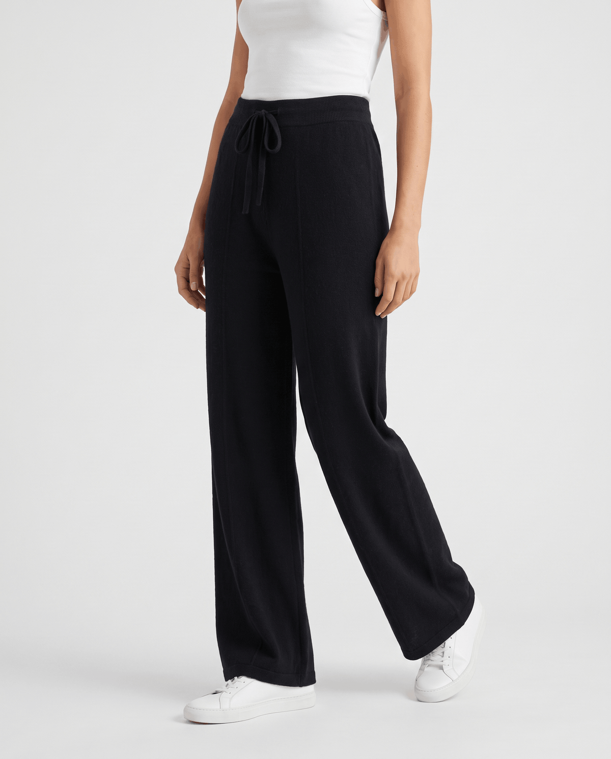 Black knit pants in three-quarter view with drawstring and white sneakers
