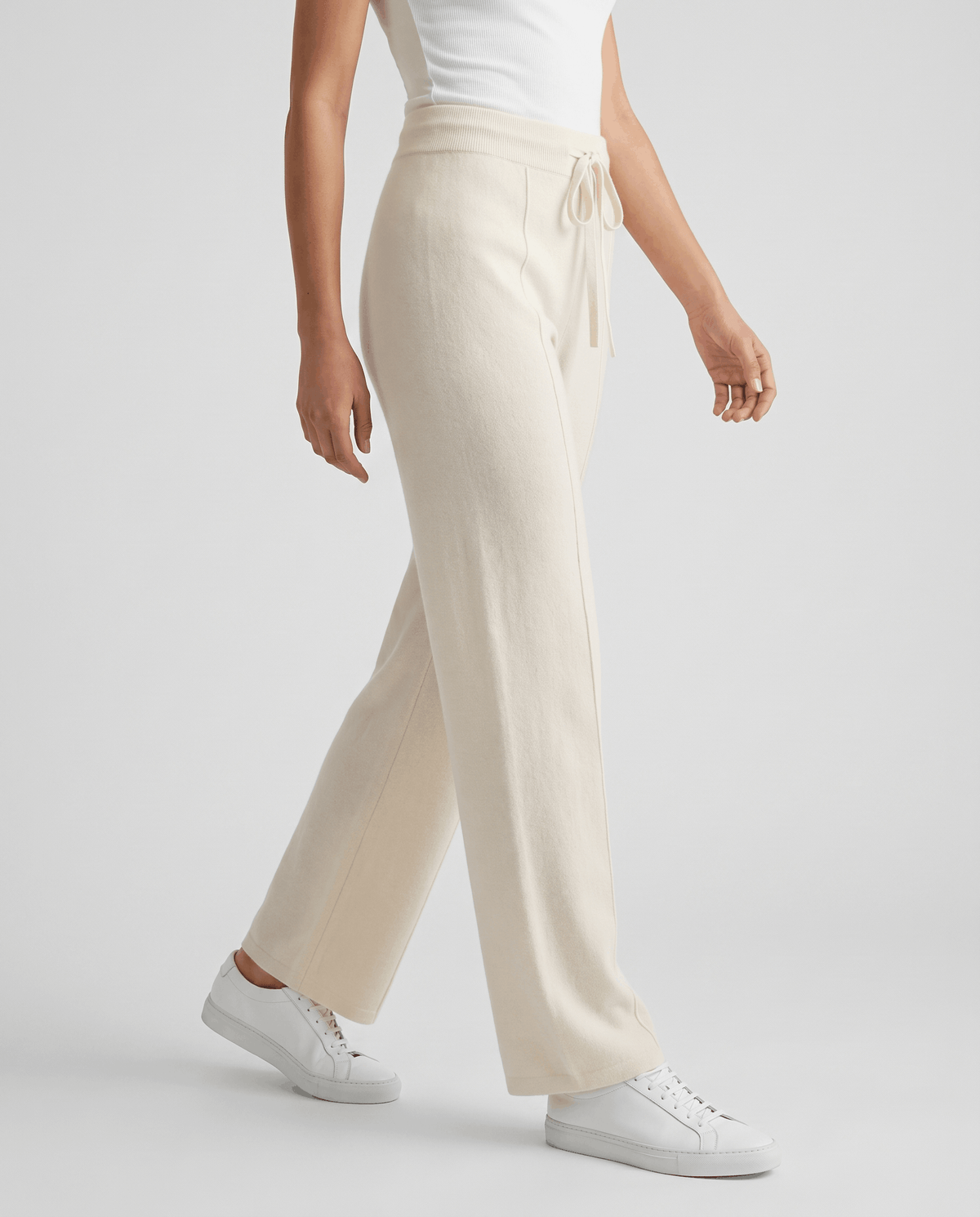Ivory knit pants in side view mid-stride with white sneakers