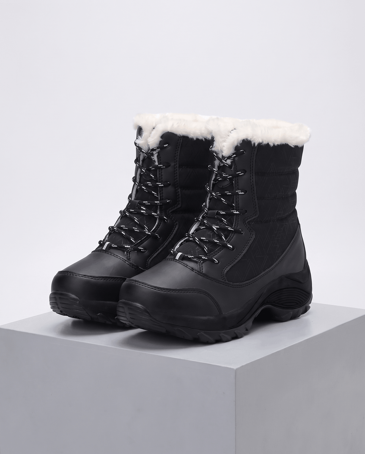 Black lace-up boots with plush white collars and thick black platform soles on grey plinth