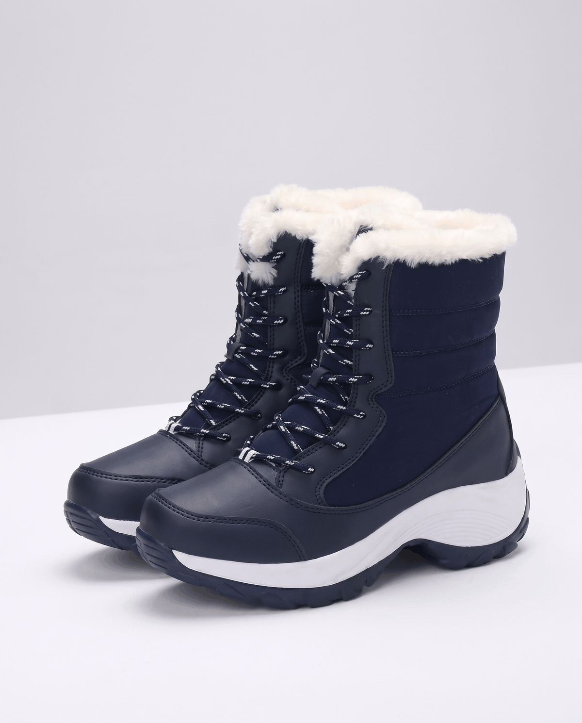 Navy blue lace-up boots with plush white collars and chunky white platform soles on light backdrop