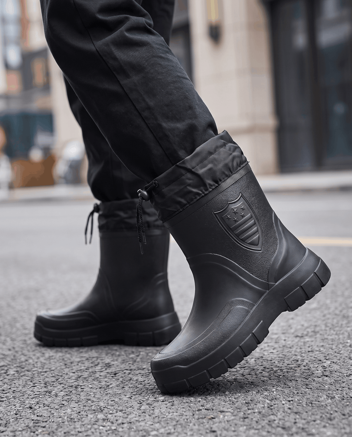 Man wearing black short boots with dark jeans on wet pavement