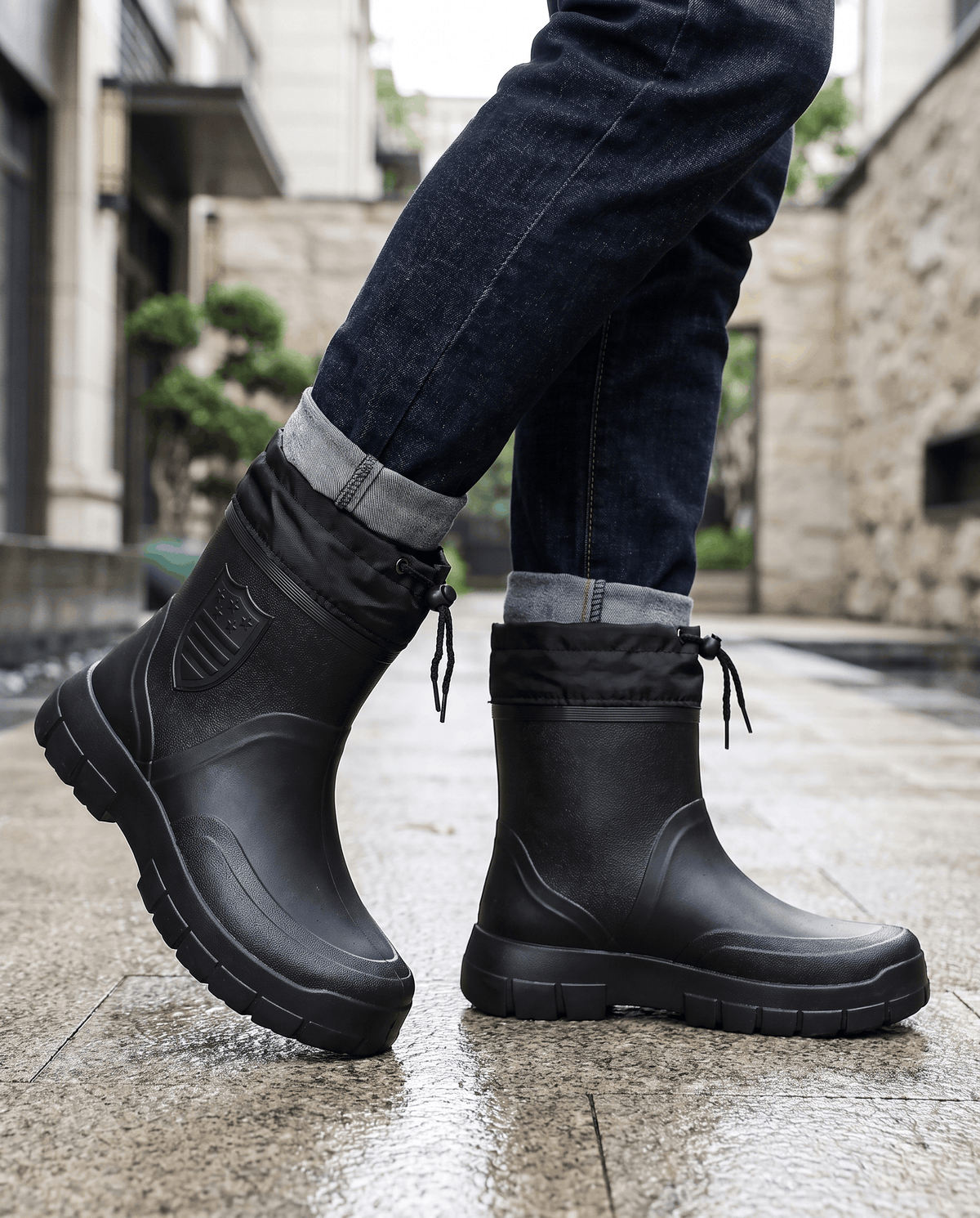 Man walking in black cord-collar boots and dark jeans on a wet street