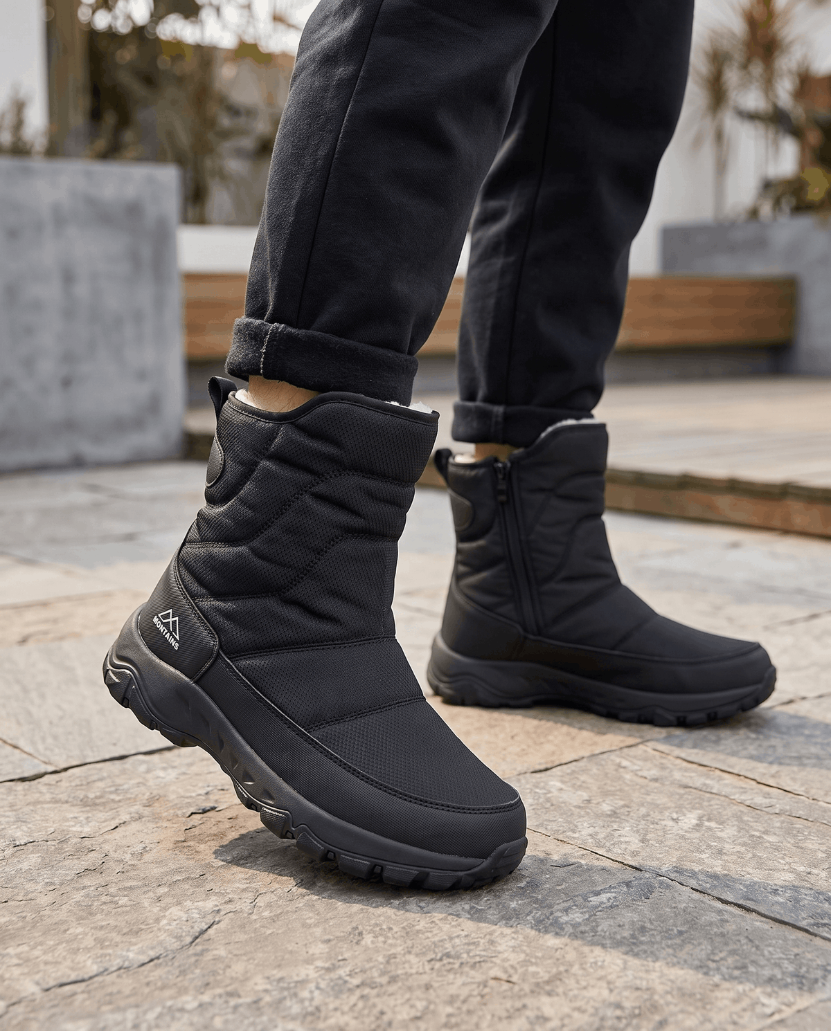 Man wearing black snow boots with dark jeans while walking on a paved street