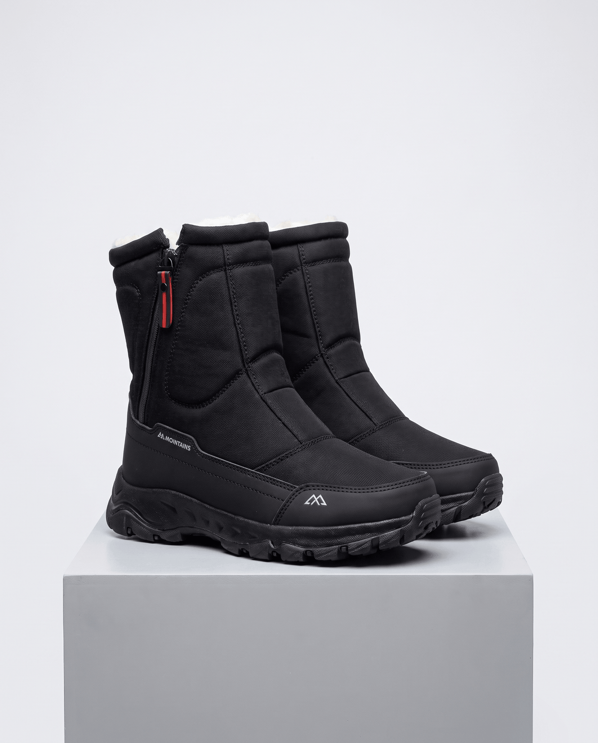 Black boots with red zipper pulls and quilted uppers standing on a grey plinth
