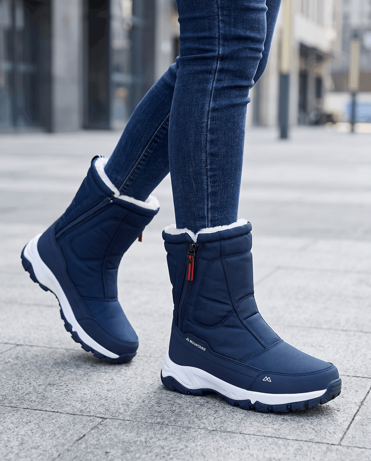 Navy blue snow boots with white-edged soles worn with jeans on a wet street