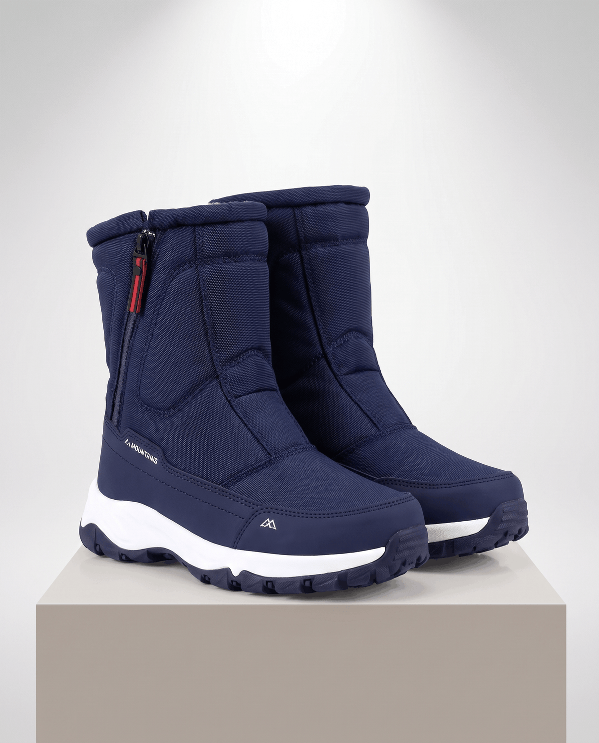 Navy blue quilted boots with white midsoles and red zipper pulls on a beige plinth
