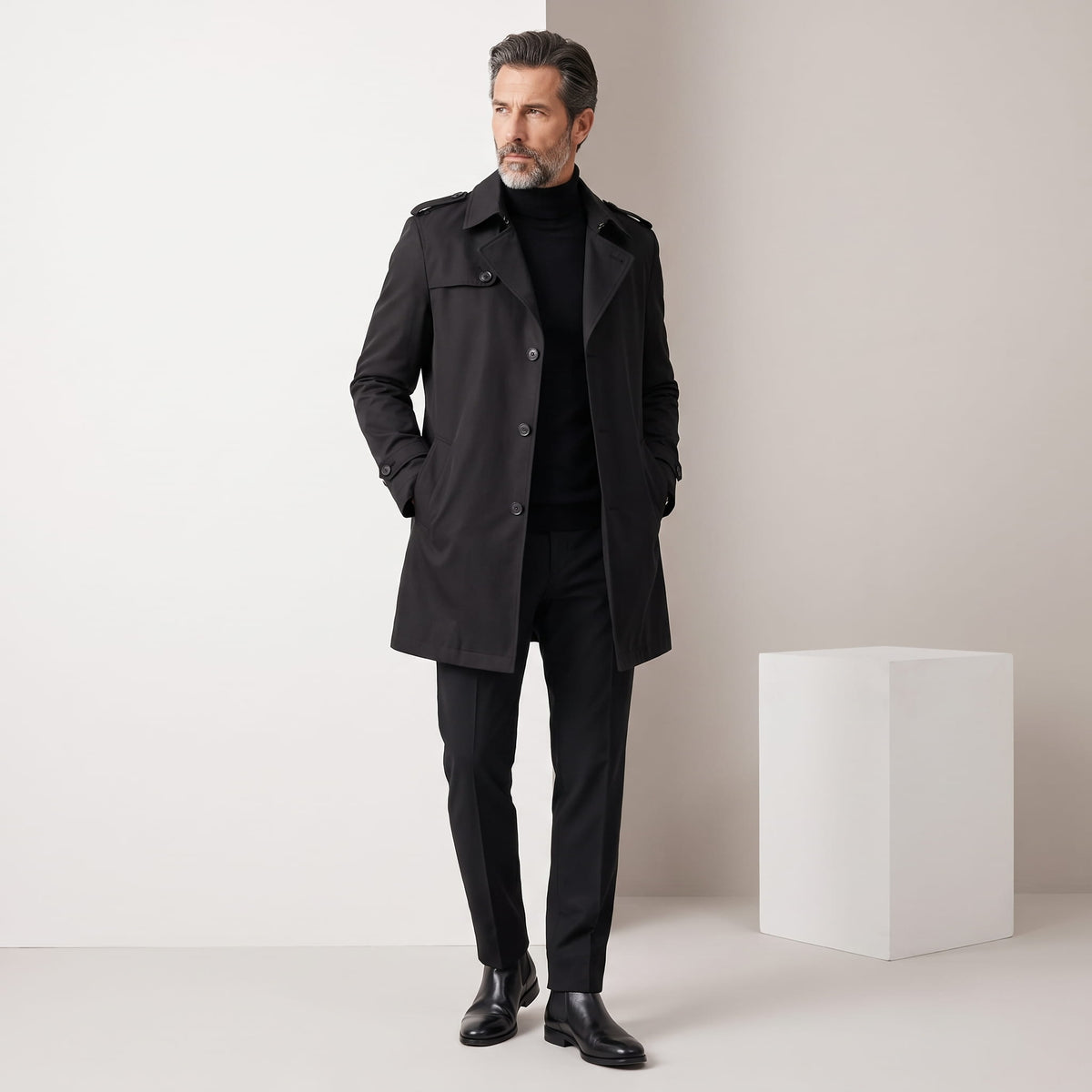 Full-length black trench coat styled with black turtleneck and trousers against a studio backdrop