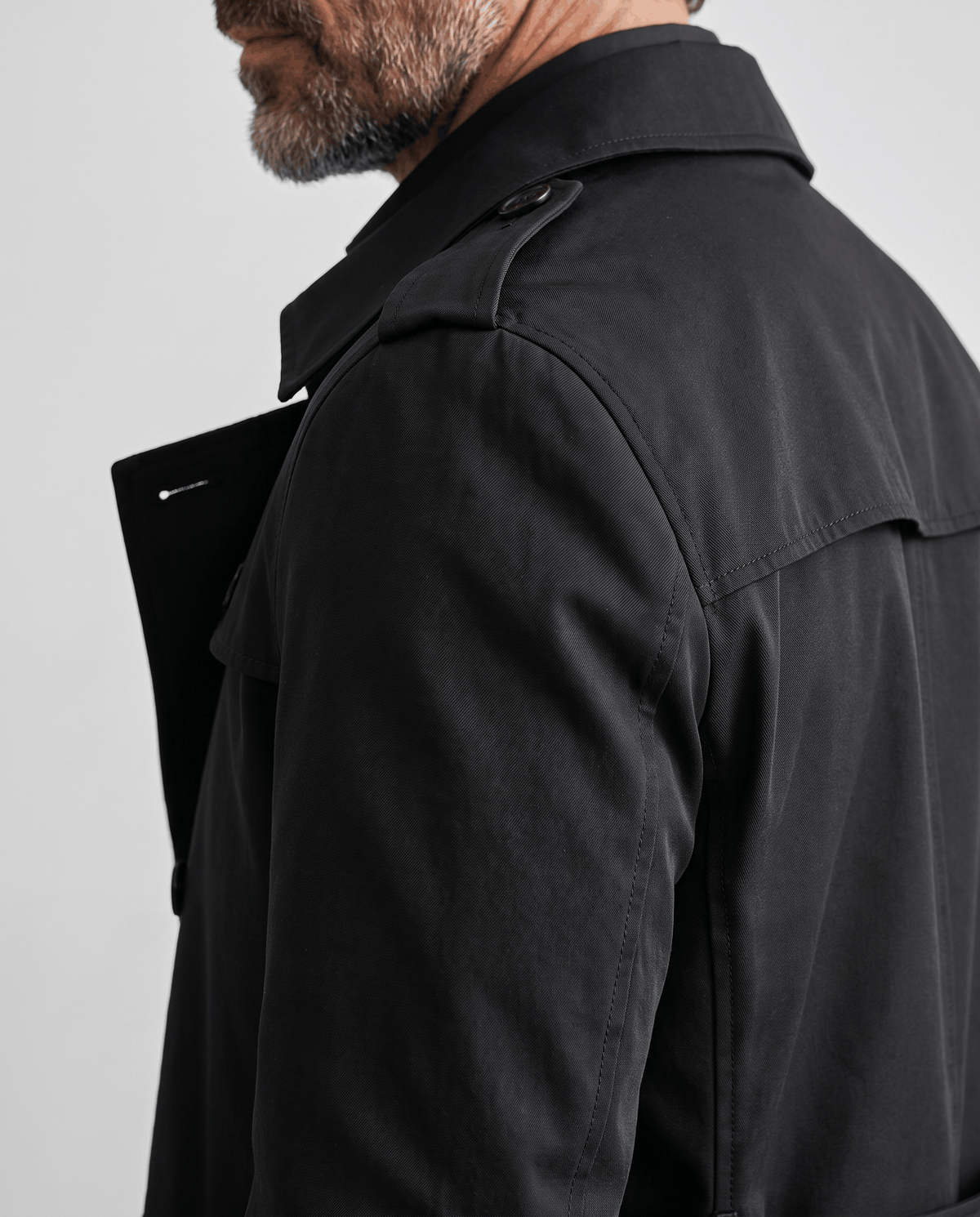 Side view of black trench coat showing shoulder epaulet and sleeve