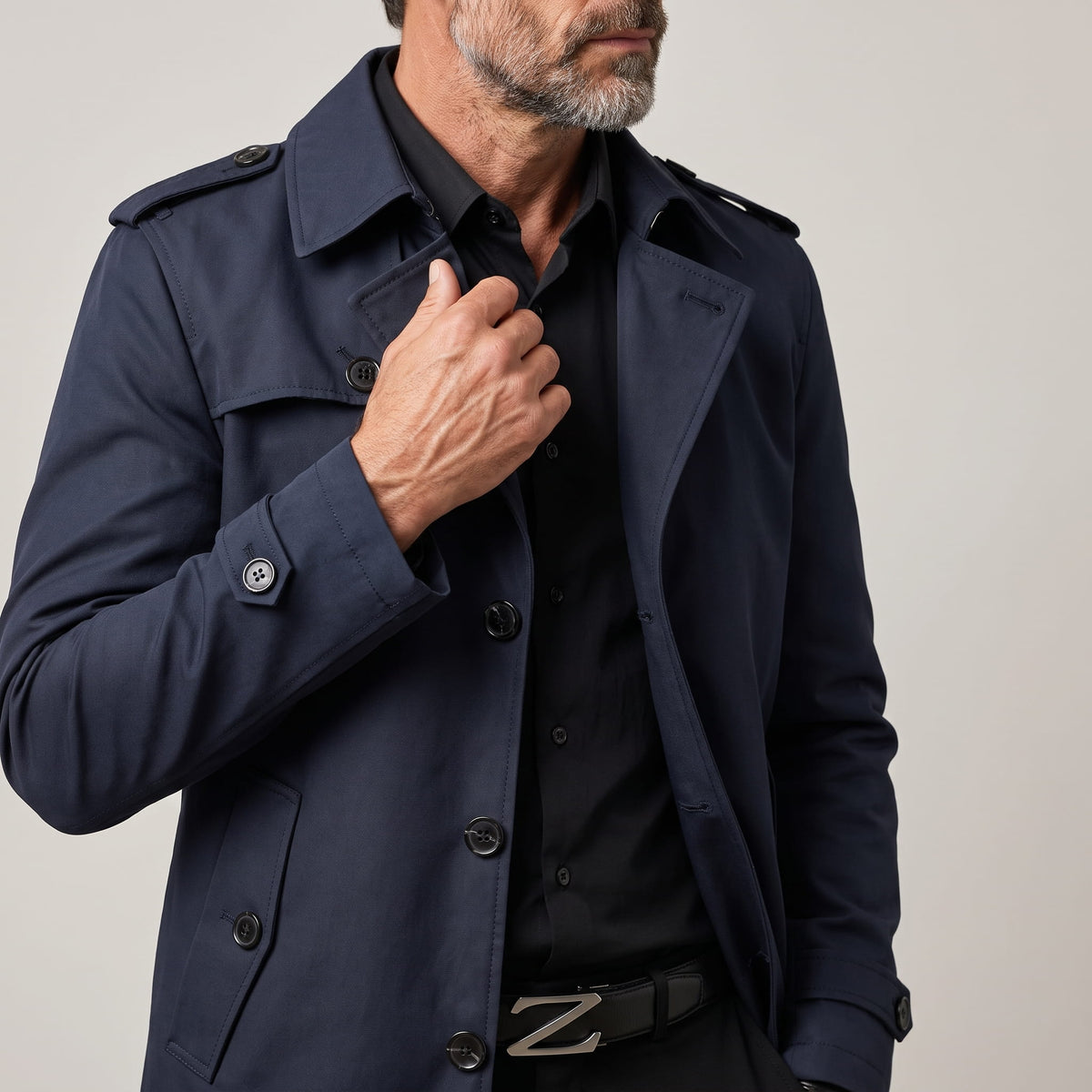 Close-up of navy blue trench coat collar and button front, model holding the lapel