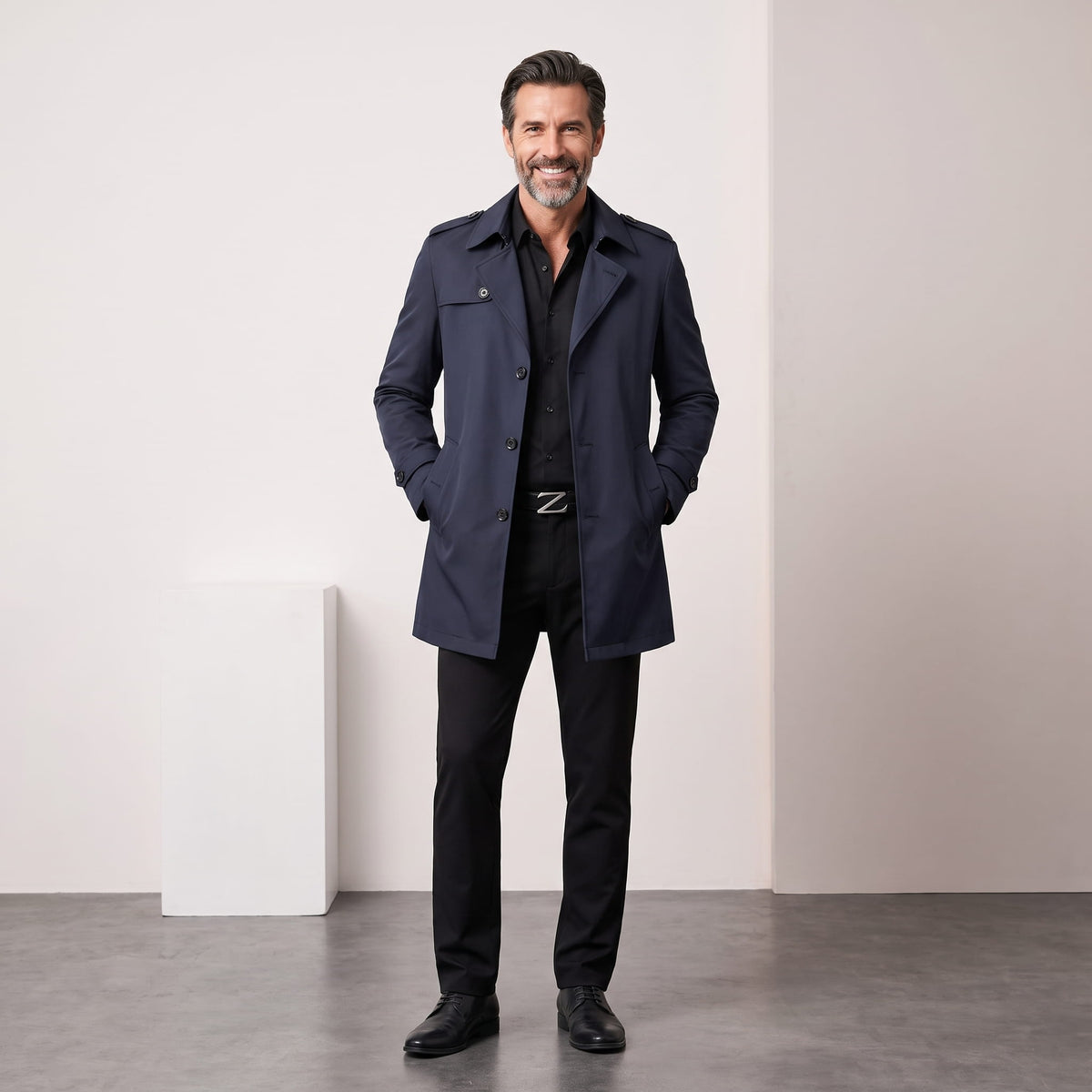 Full-length navy blue trench coat worn with dark trousers against a studio backdrop