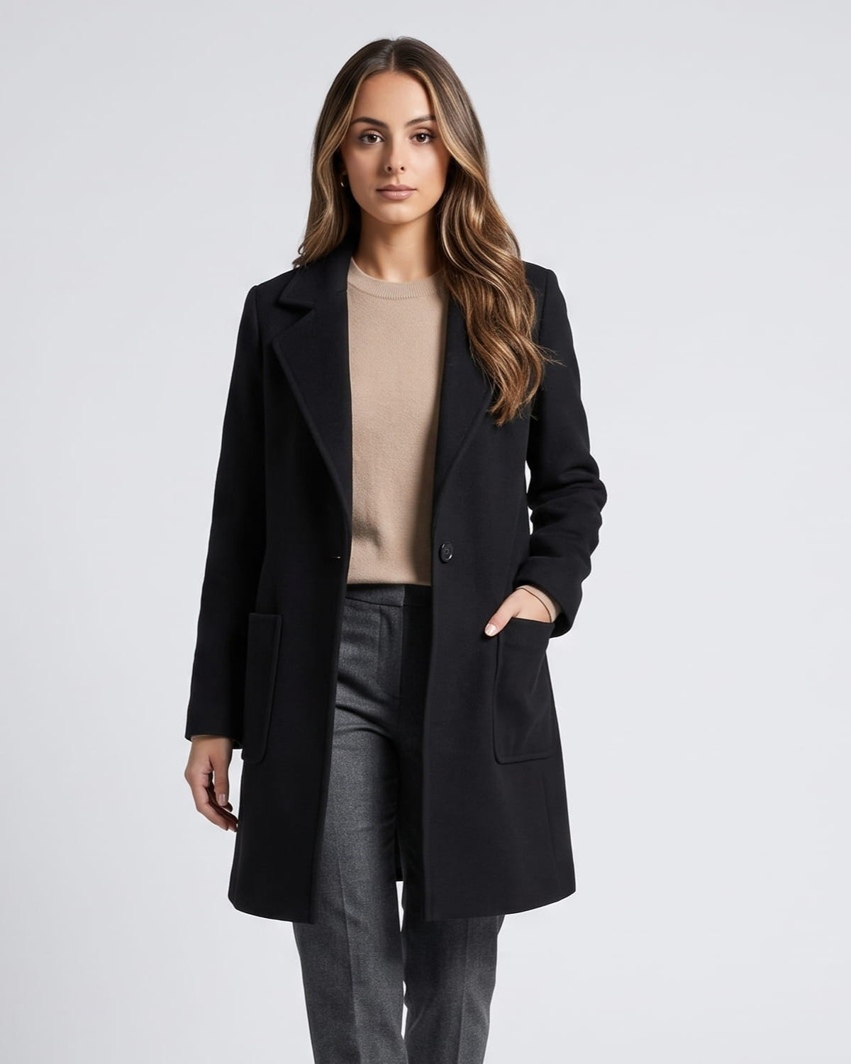 Woman in black mid-length wool coat with notched lapels, beige sweater and gray jeans