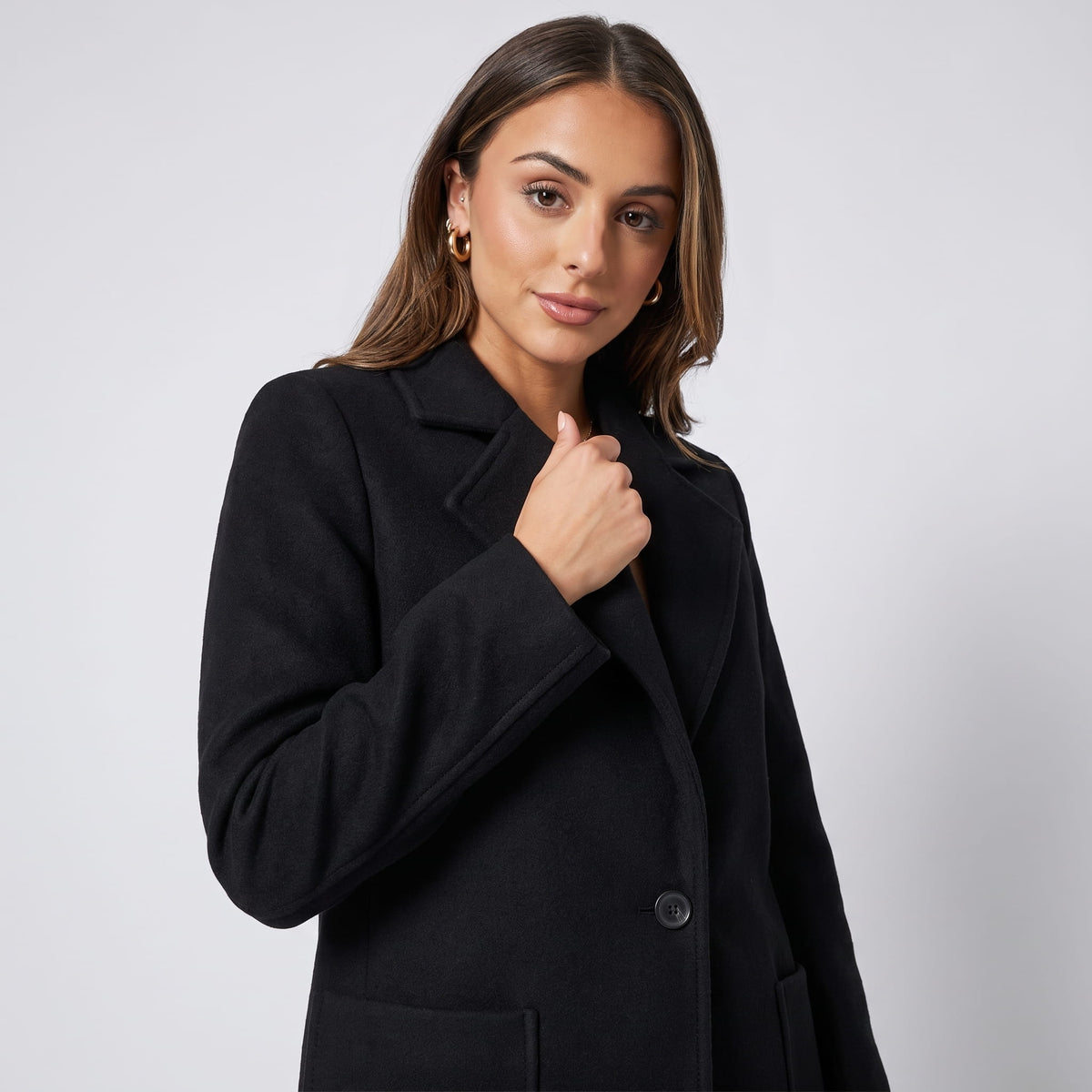 Three-quarter view of black coat worn with one hand resting on the lapel